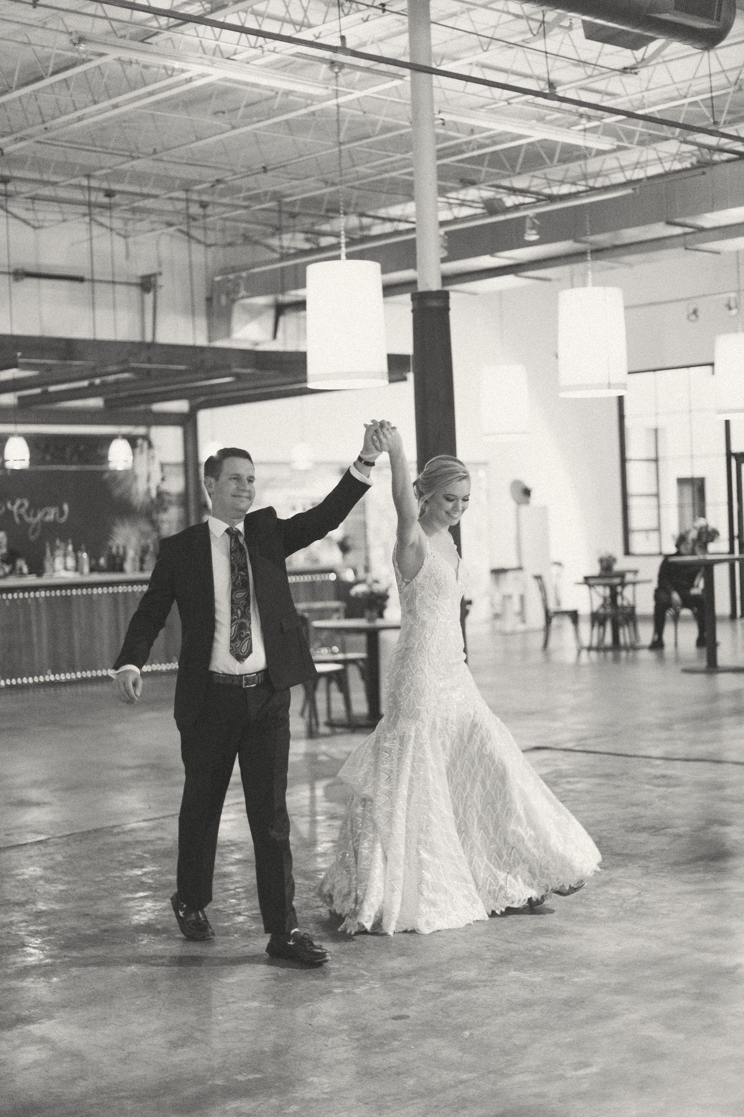 Bride and groom share first dance in black and white photo in spacious industrial reception venue.