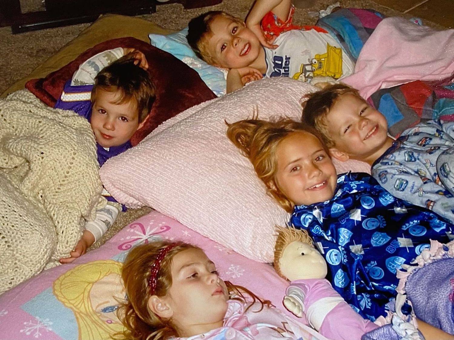 Five children snuggled together in sleeping bags and pillows during a cozy sleepover.