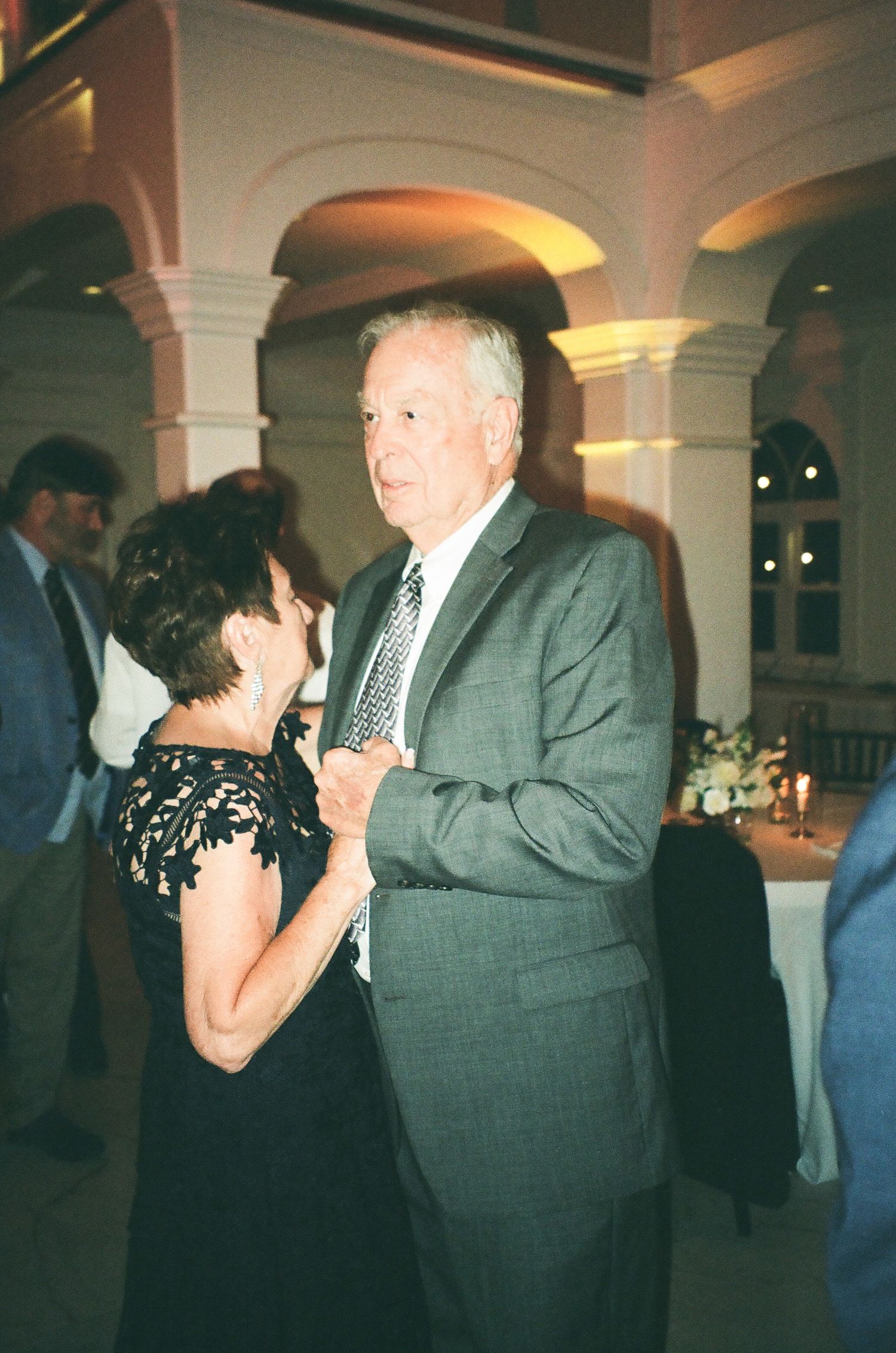 Elegant couple slow dancing at a wedding reception in a grand venue with arched columns.
