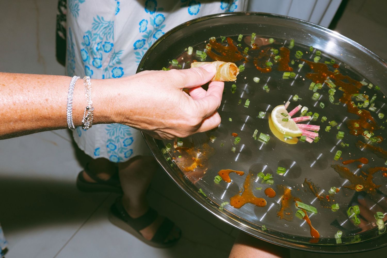 A hand squeezing lemon into a large metal bowl of broth with green onions, preparing a flavorful soup.