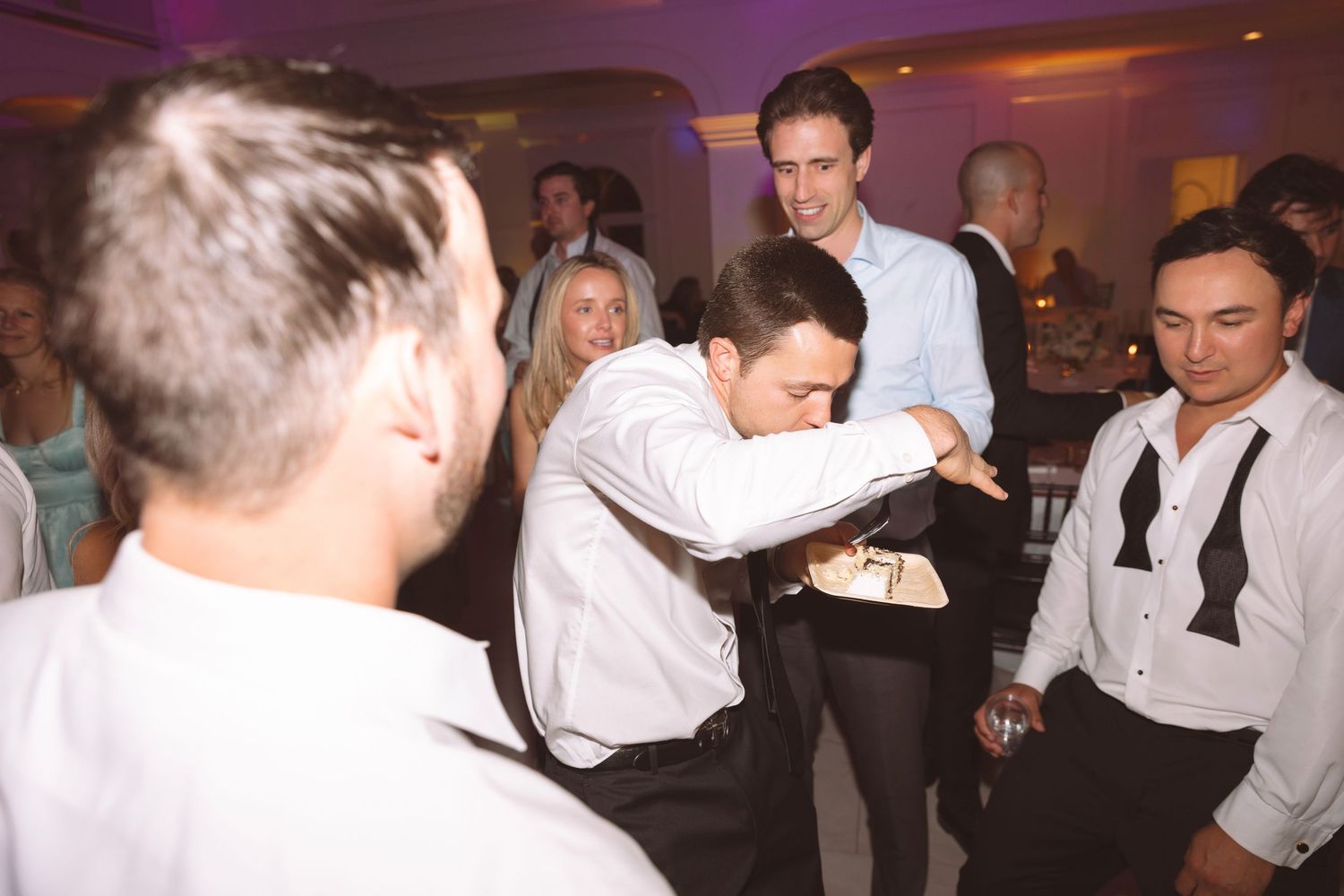 Men in formal attire dancing and celebrating at an elegant wedding reception party.