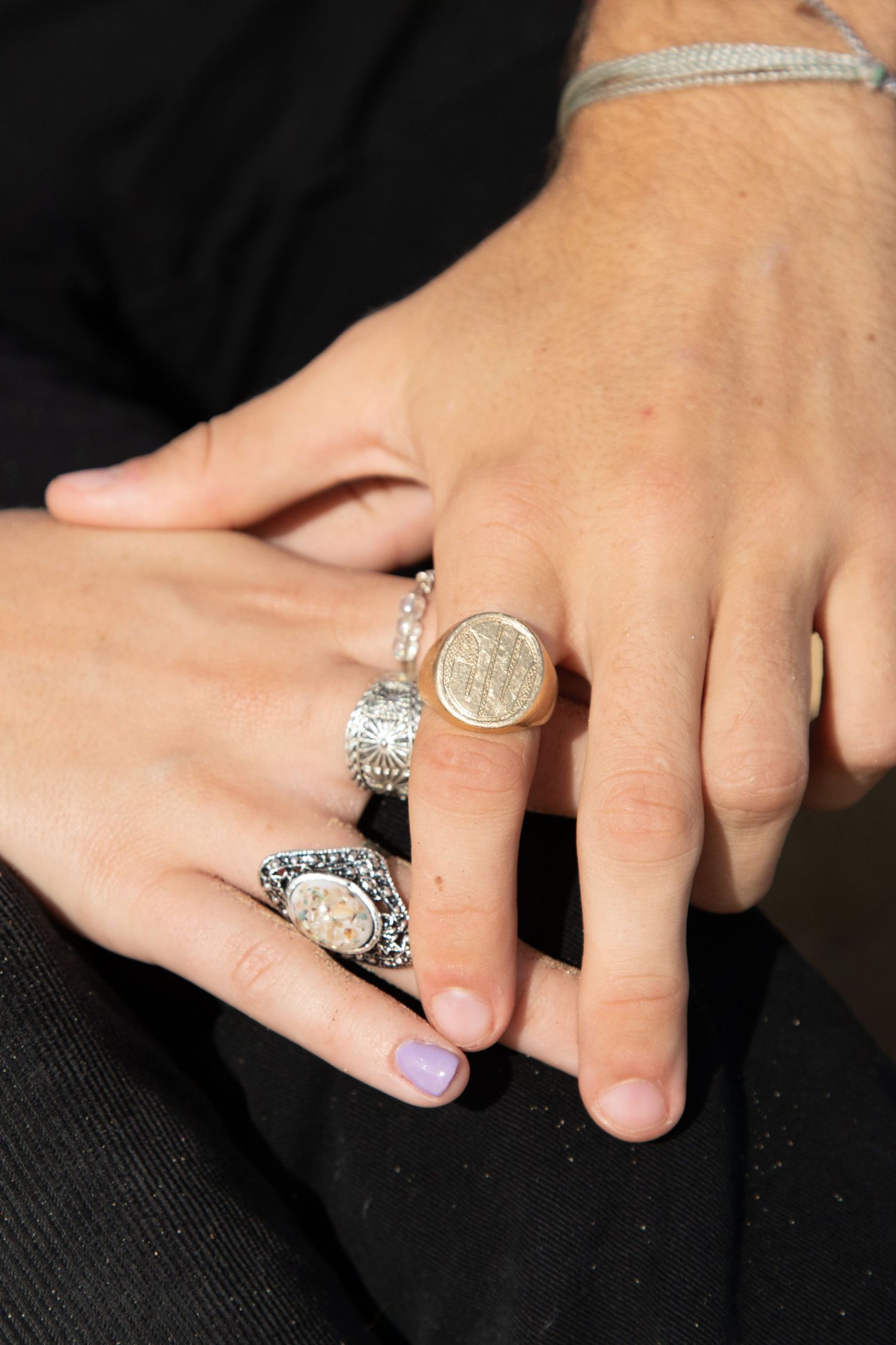 Close-up of two hands together adorned with decorative silver and gold rings and bracelet.