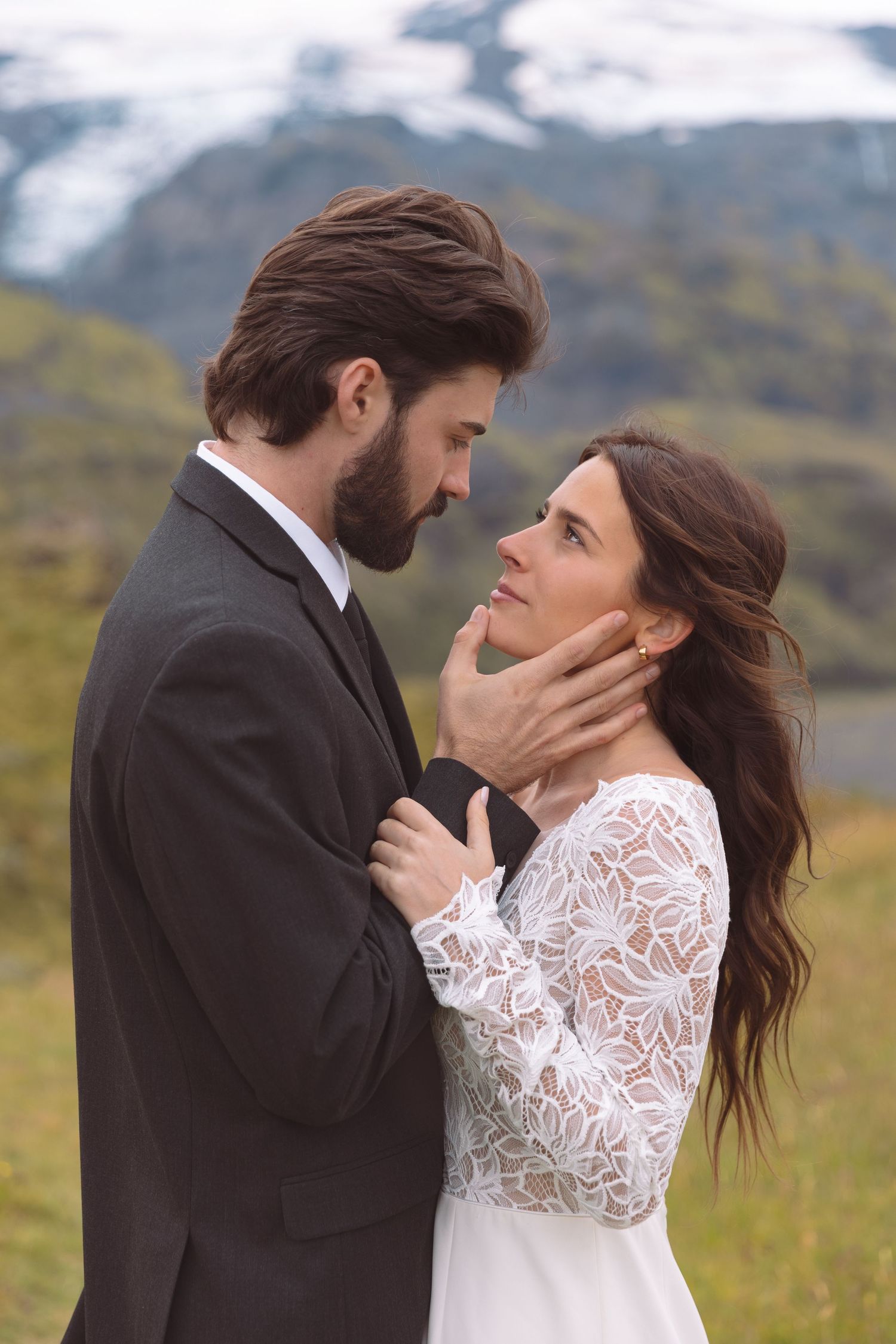 Groom tenderly holding bride's face as they gaze into each other's eyes with Icelandic glacier behind.