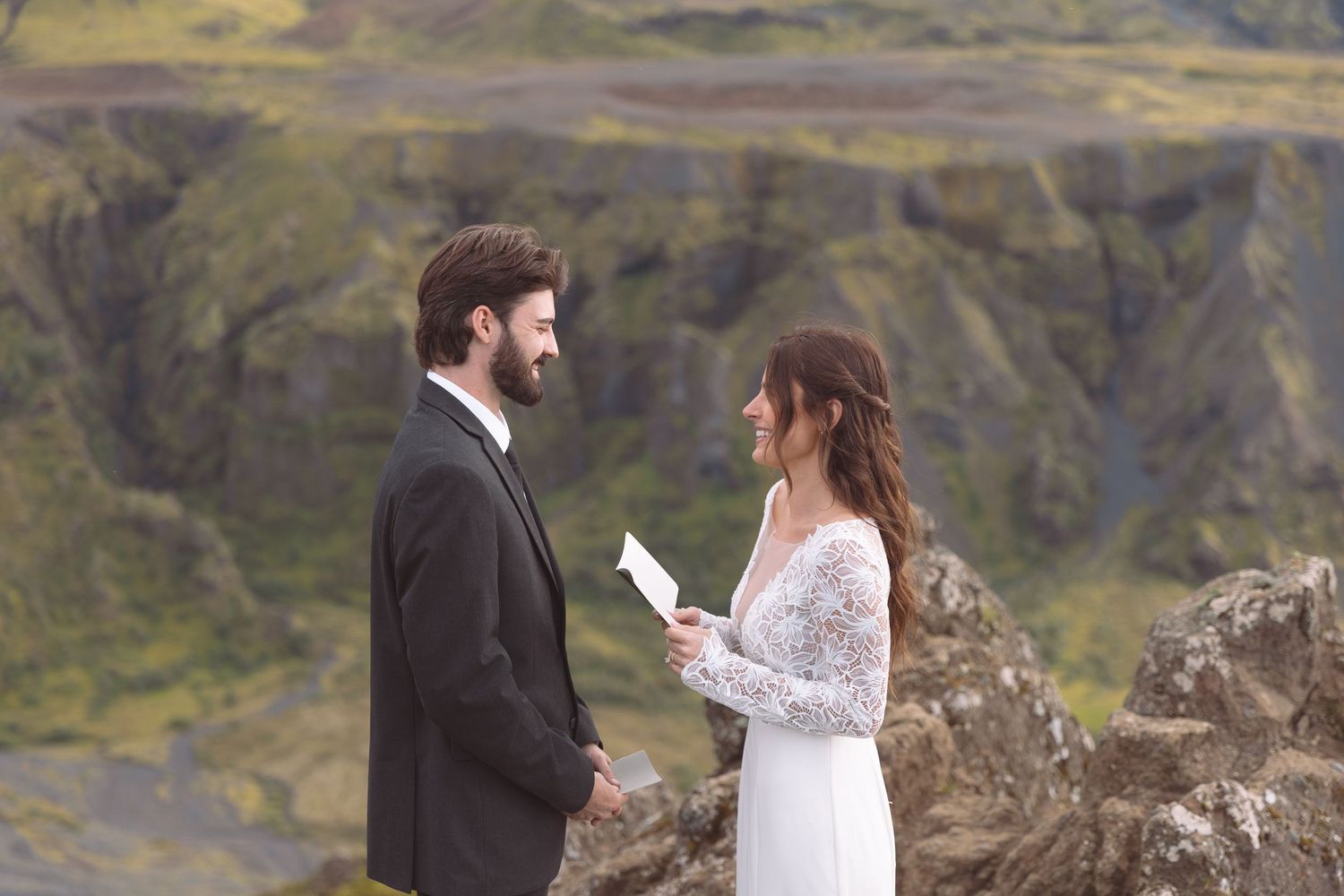 Bride reads wedding vows to groom on rocky mountain cliff during outdoor elopement ceremony in Iceland.