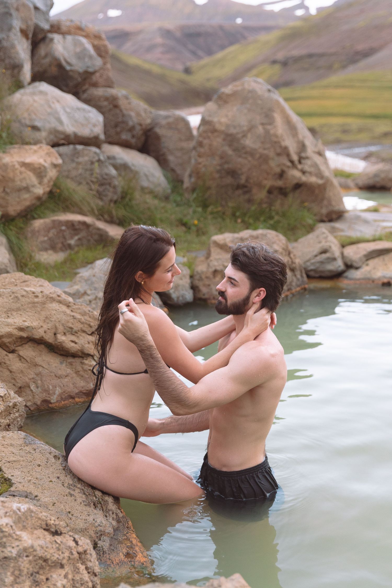 Couple in swimwear holding each other tenderly in a rocky Icelandic hot spring.