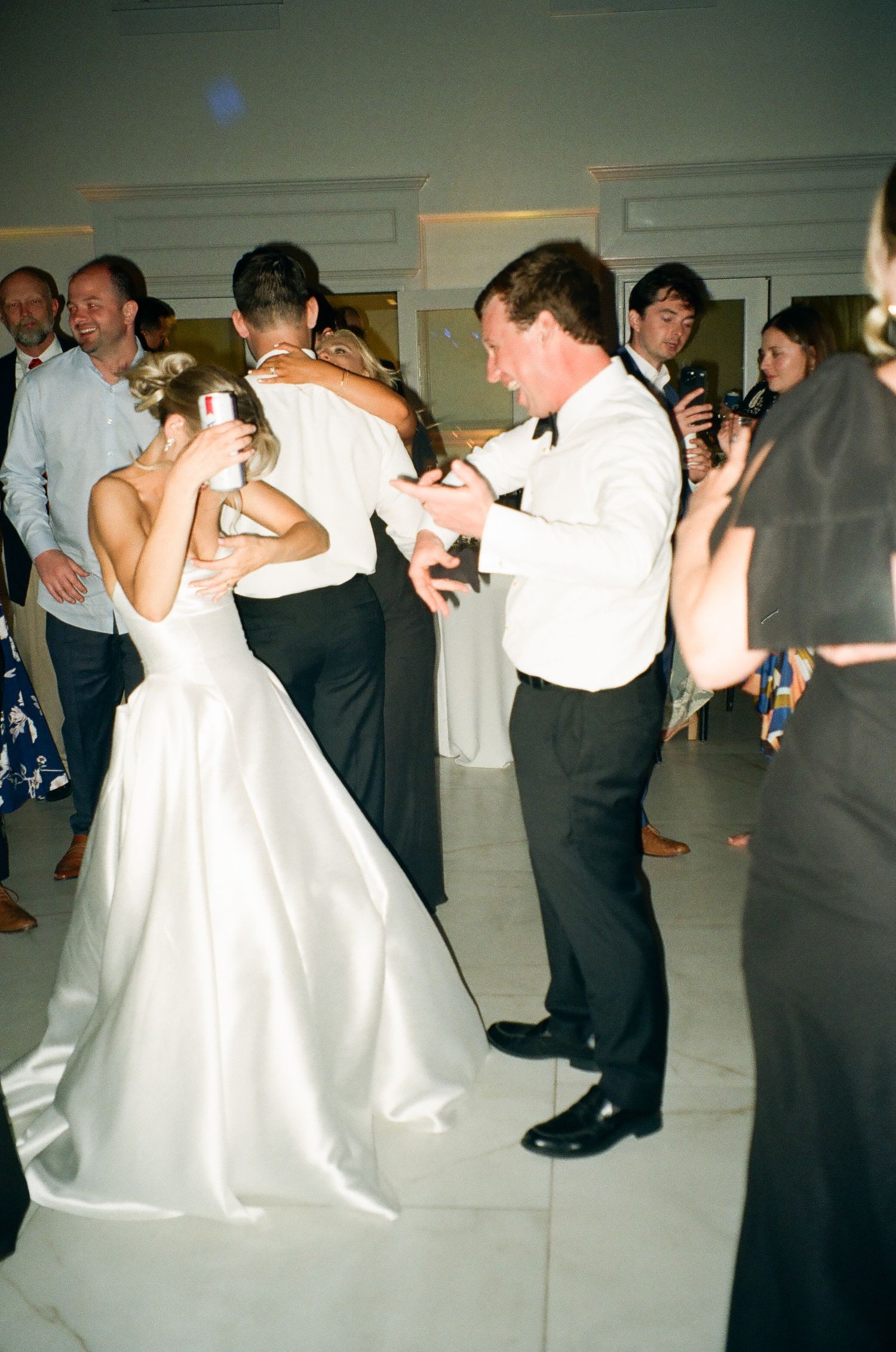 Bride in white gown dancing with guests in formal attire at elegant wedding reception.