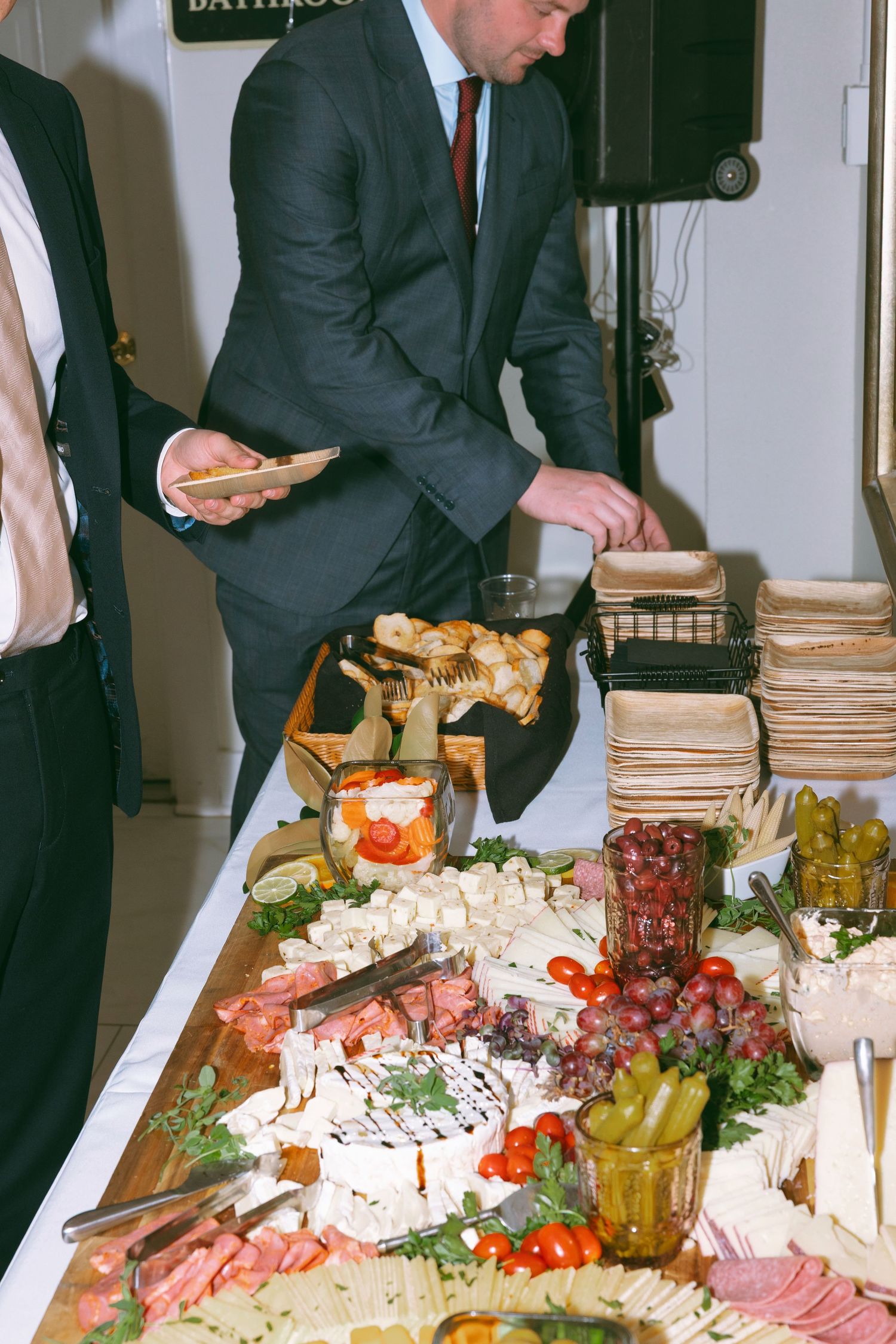 Elegant charcuterie board with cheese, meats, tomatoes, and pickles at a formal catered event with guests serving themselves.