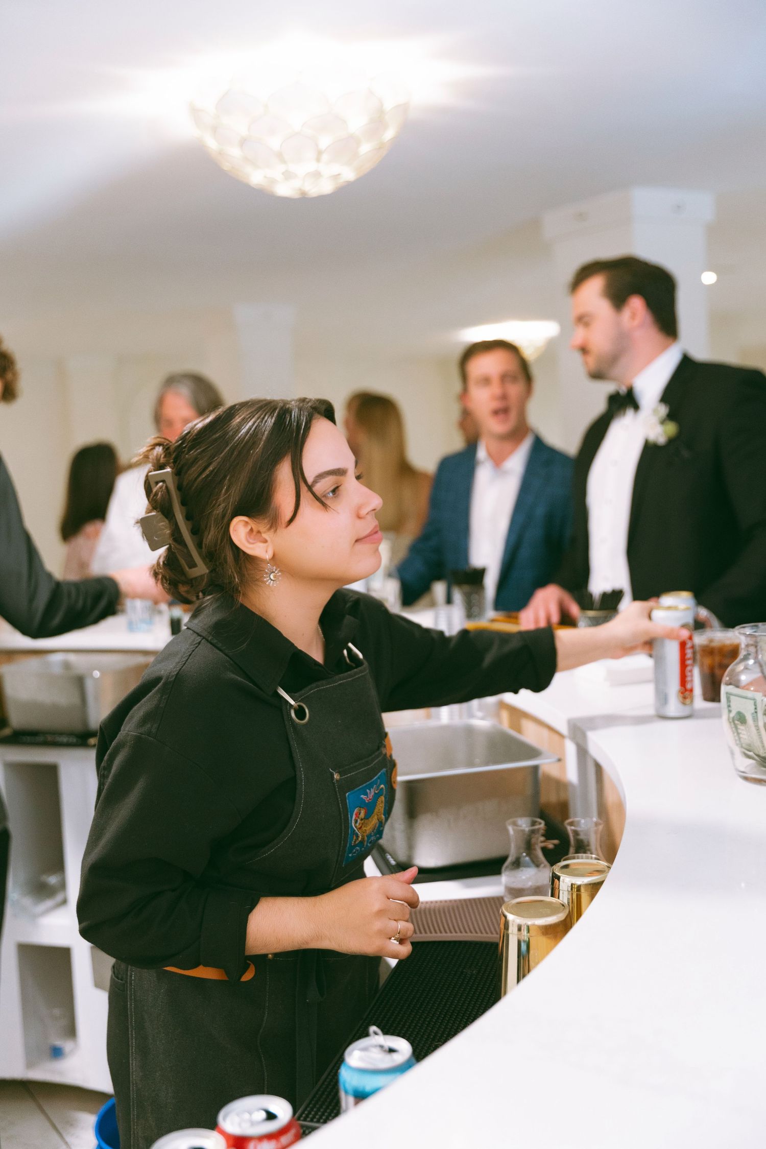 Female bartender in black apron serving drinks at a wedding reception bar.