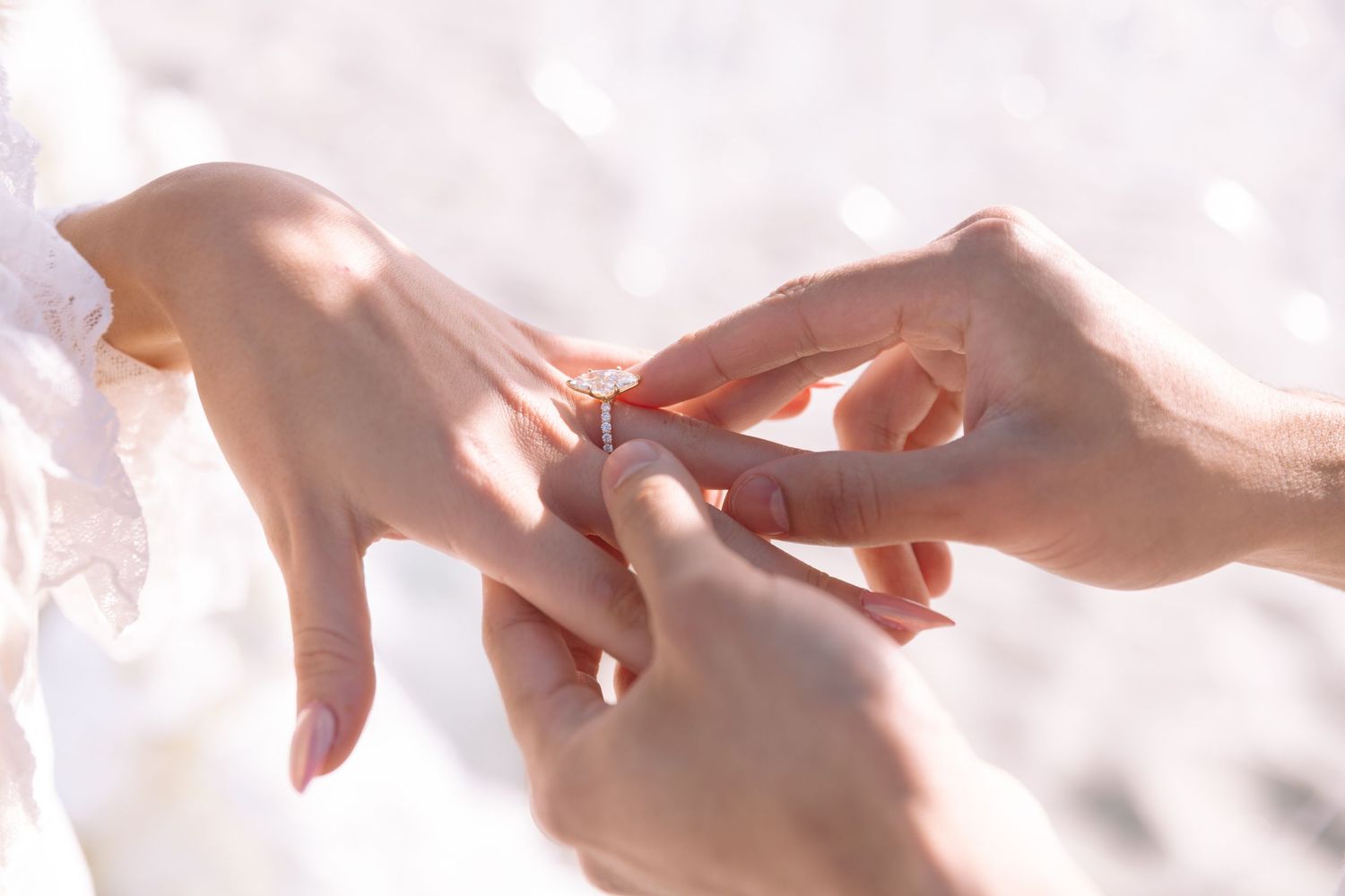 A person placing a diamond engagement ring on their partner's finger during a romantic outdoor wedding ceremony.