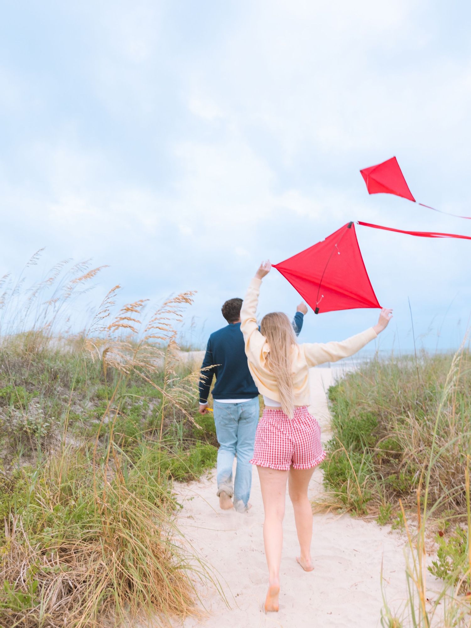Couple running toward beach dunes while flying red kites on a sunny day.