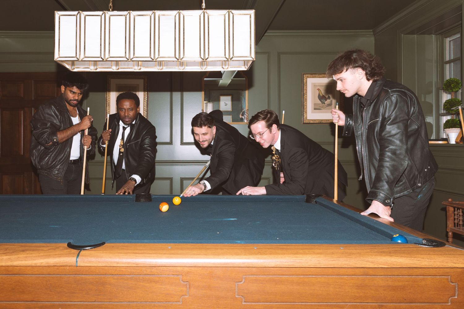 Groomsmen and guests play pool together in a wood-paneled room before the wedding reception.