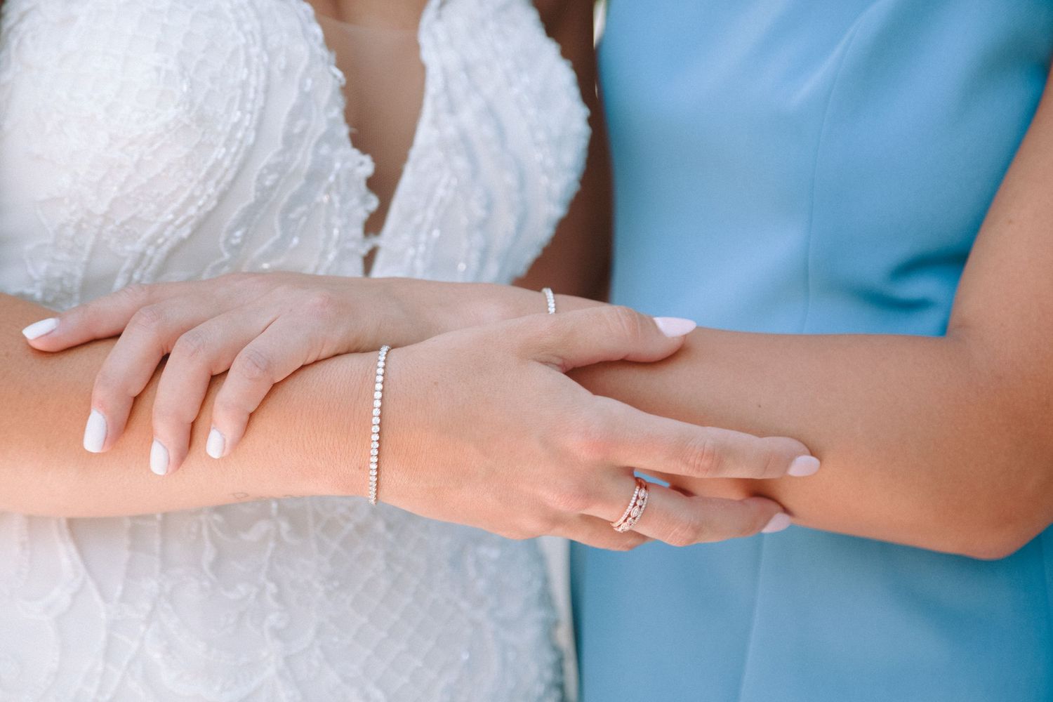 Close-up of bride and bridesmaid holding hands showing pearl bracelet and diamond ring on wedding day.