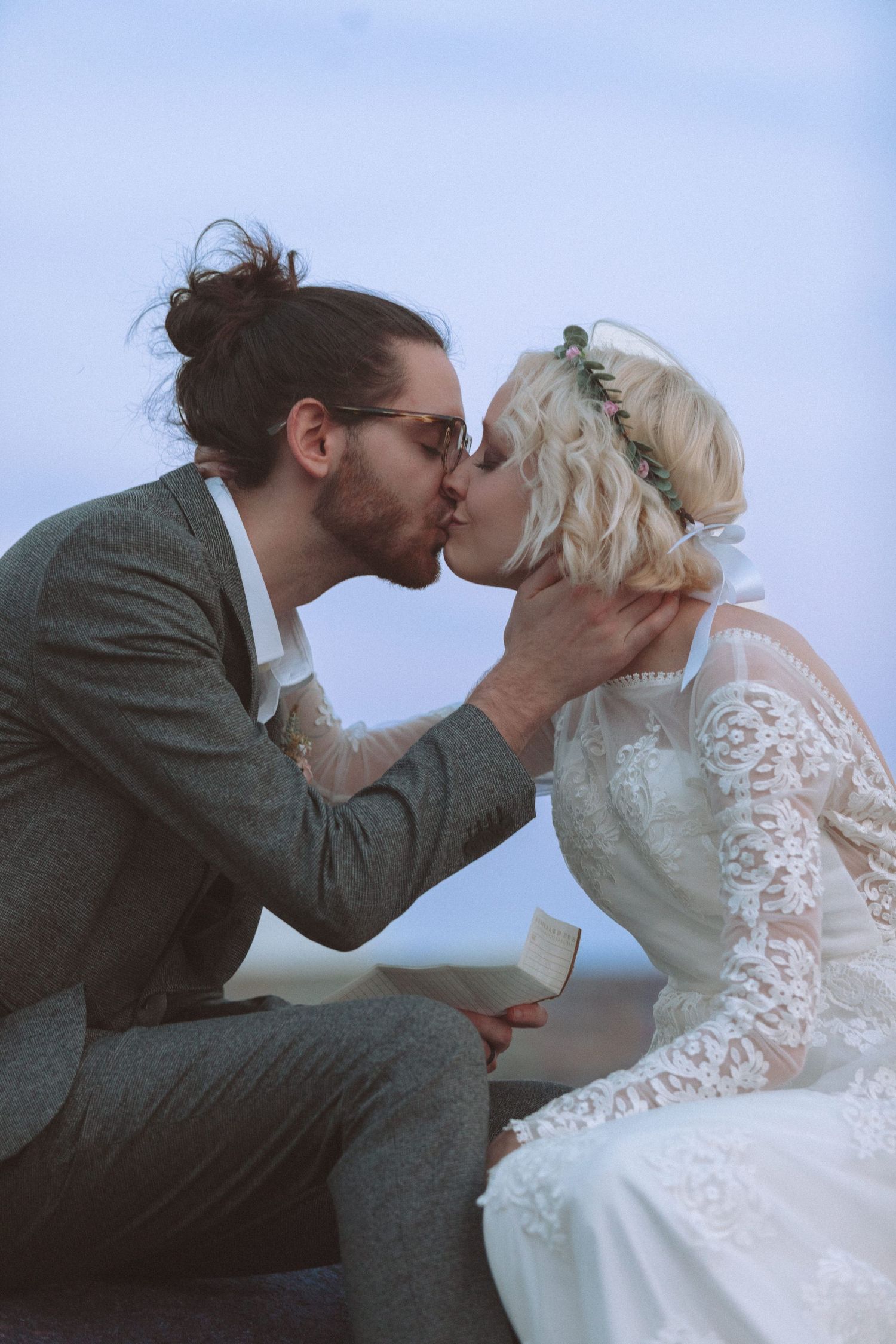 Bride and groom sharing a romantic kiss outdoors on their wedding day by the water.