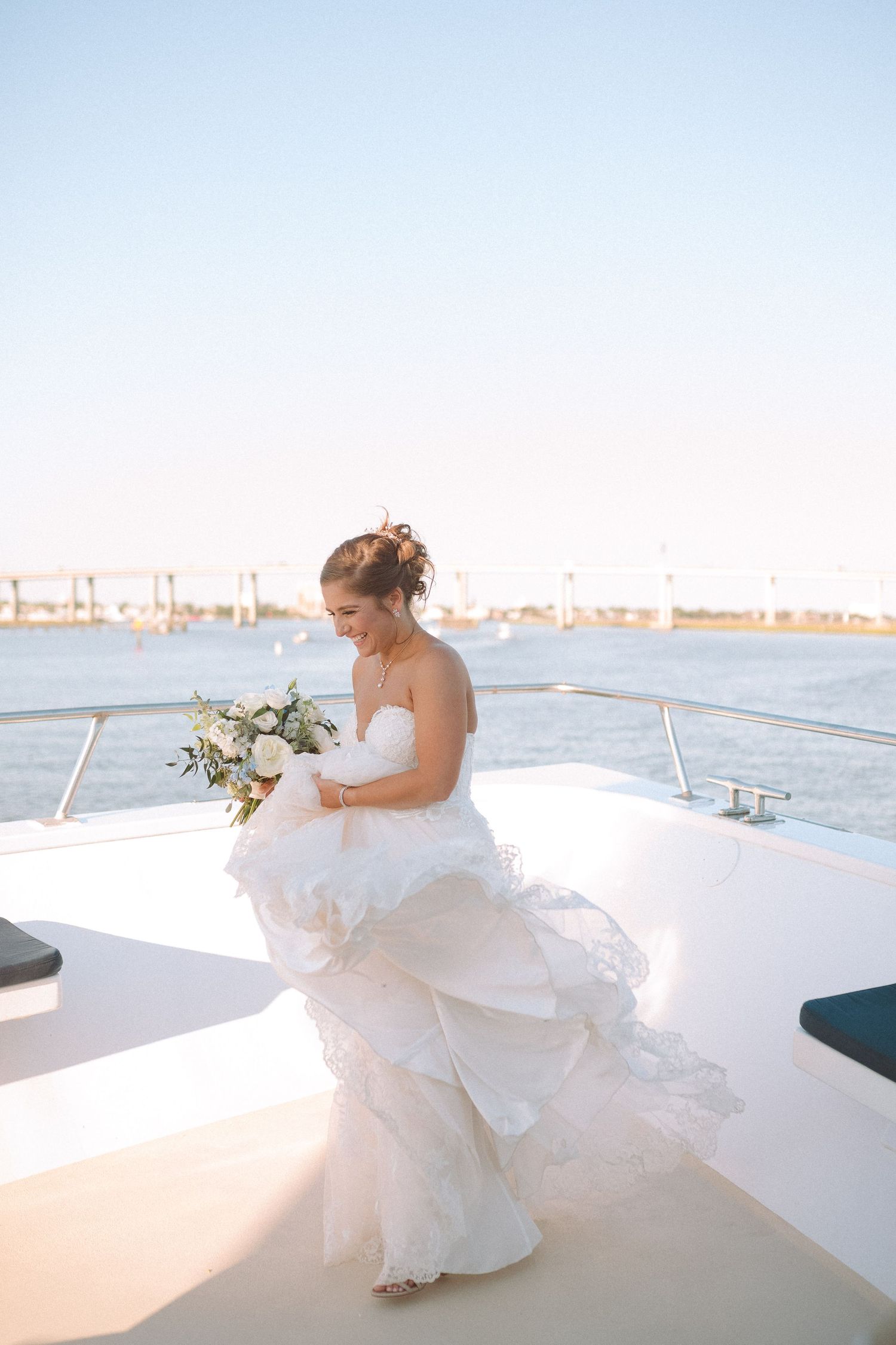 Beautiful bride in strapless ruffled wedding gown holding bouquet on luxury yacht deck.