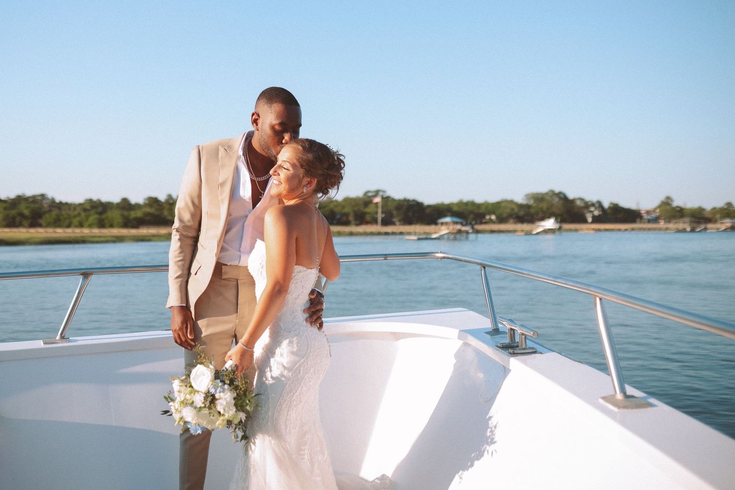 Newlywed interracial couple embracing on the bow of a yacht with scenic waterway views.