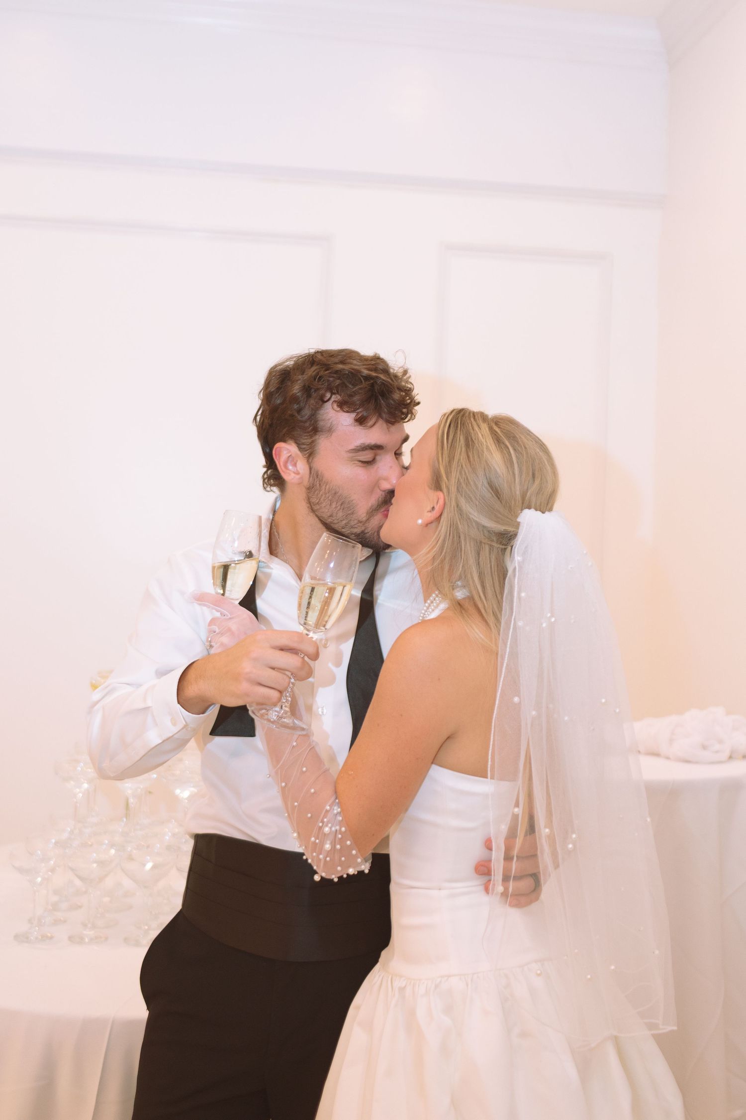 Newlyweds sharing romantic kiss while holding champagne flutes at wedding.