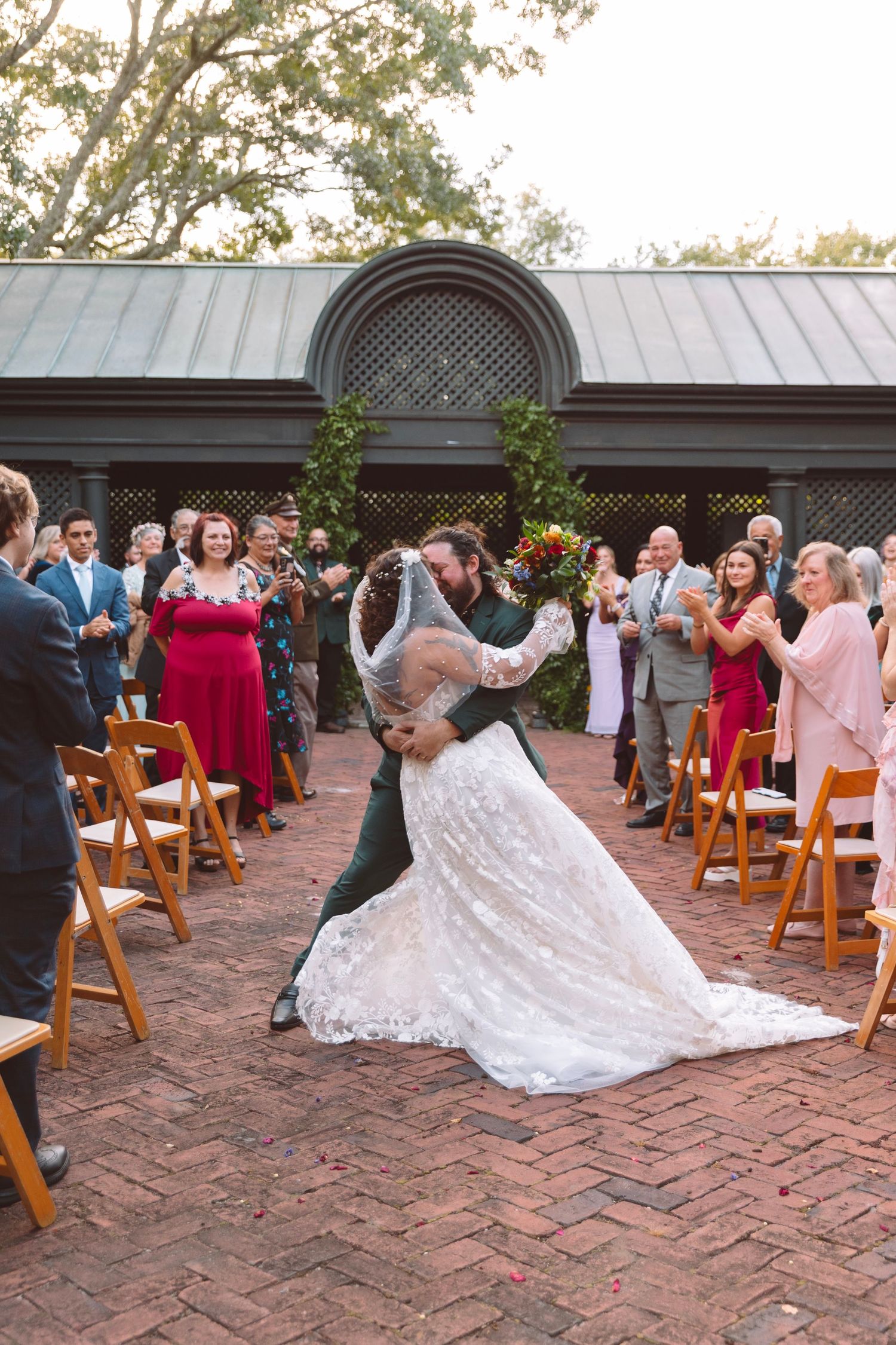 Bride and groom share a romantic dip kiss while walking down the aisle at an outdoor wedding ceremony.