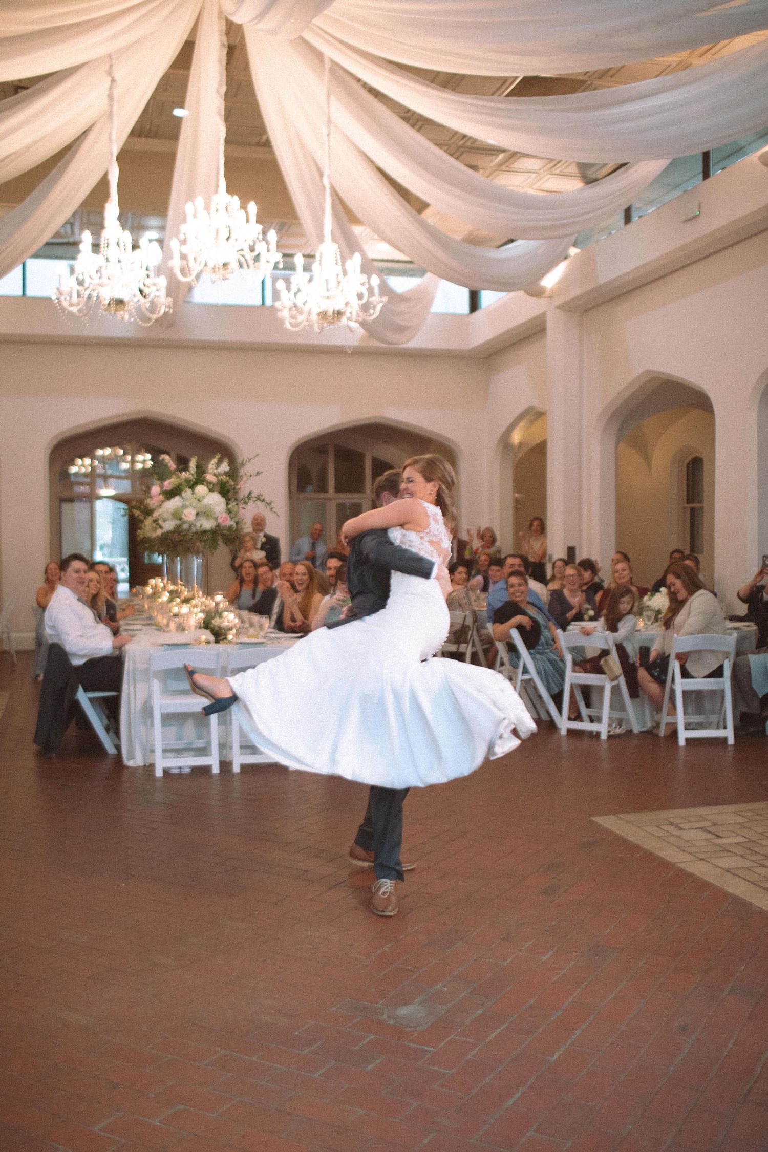 Bride and groom share a dramatic first dance spin in an elegant ballroom with chandeliers and draped ceilings.