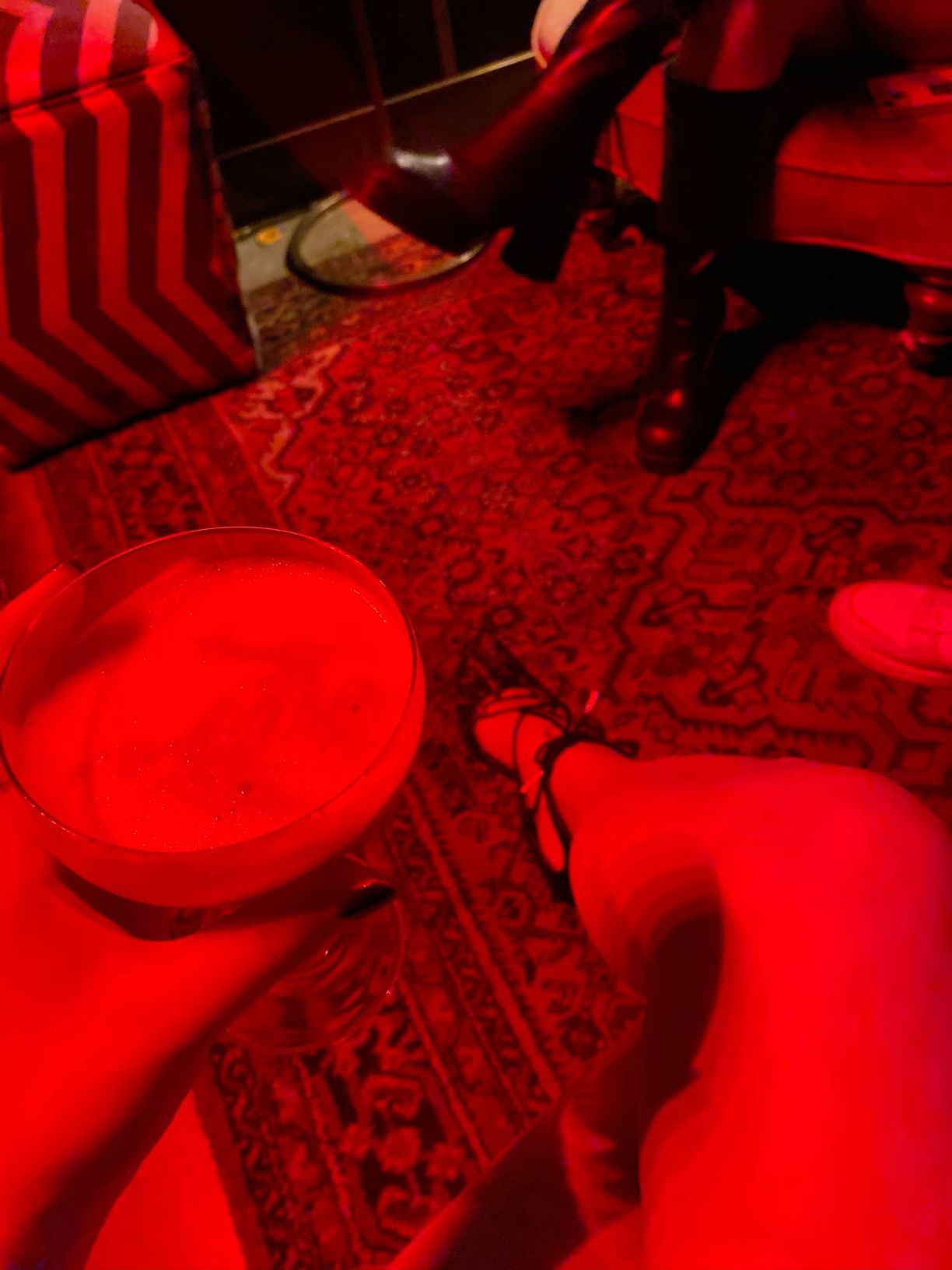 Frothy white cocktail in martini glass under dramatic red lighting in moody bar setting.