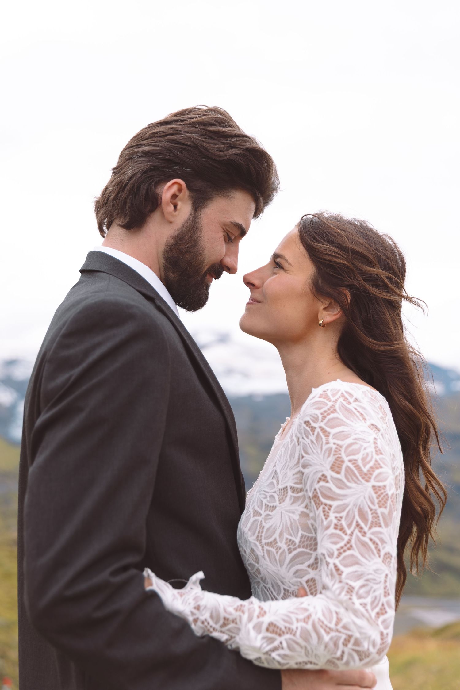 Newlywed couple shares an intimate moment nose to nose with misty mountain landscape in the background.