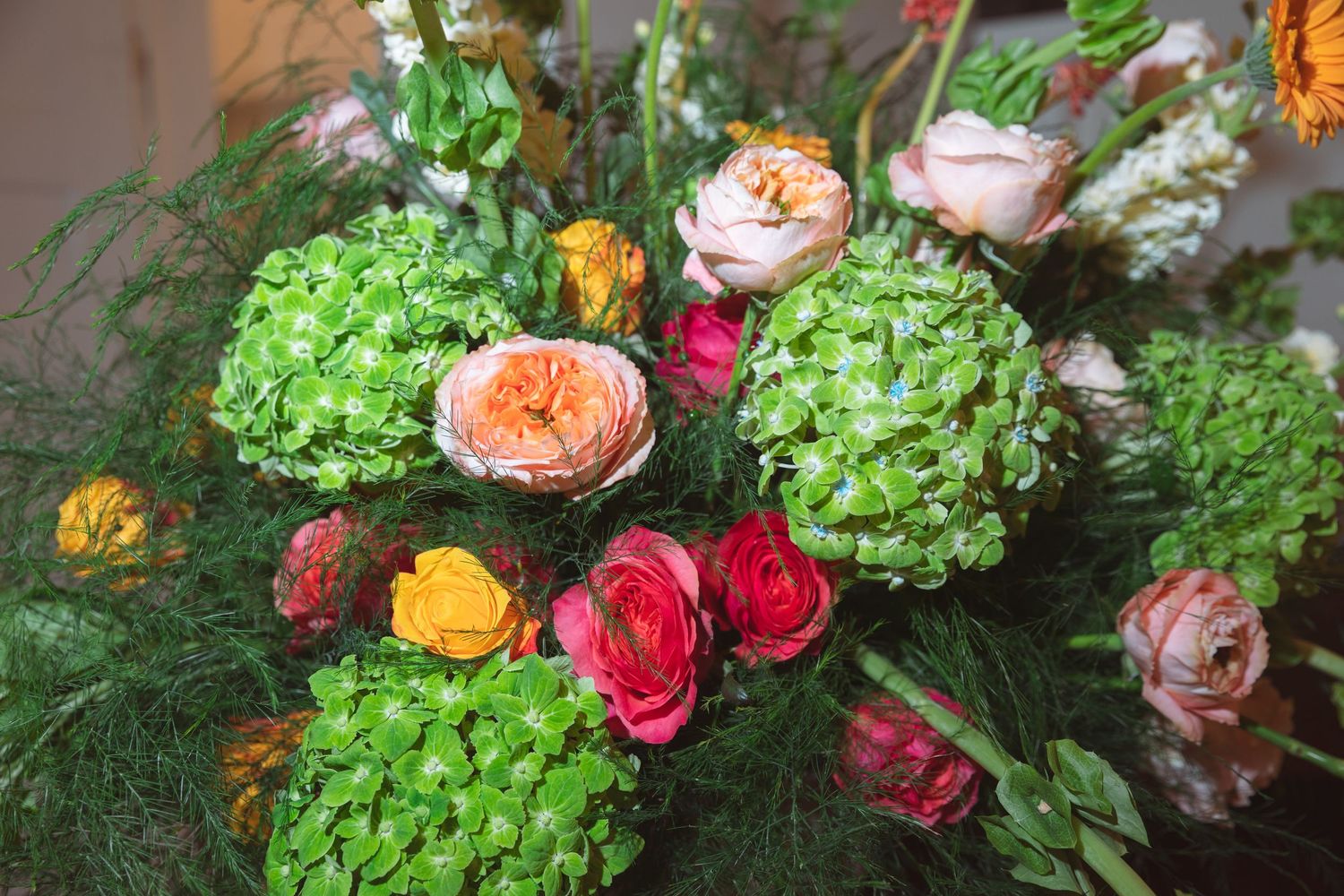 Vibrant floral arrangement featuring green hydrangeas, peach garden roses, pink ranunculus, and yellow blooms with lush greenery.