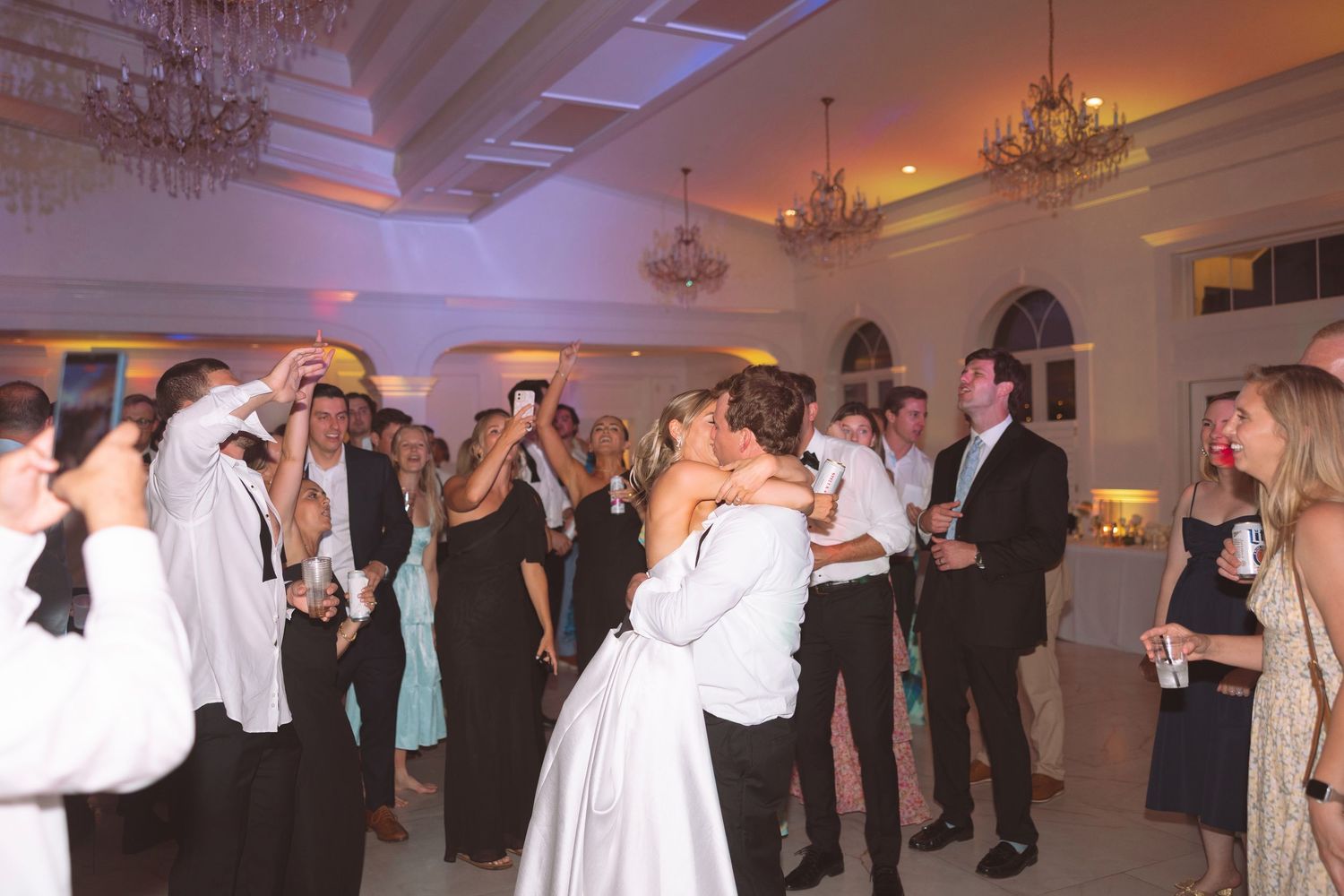 Bride and groom share first dance surrounded by guests in a grand ballroom at their wedding reception.