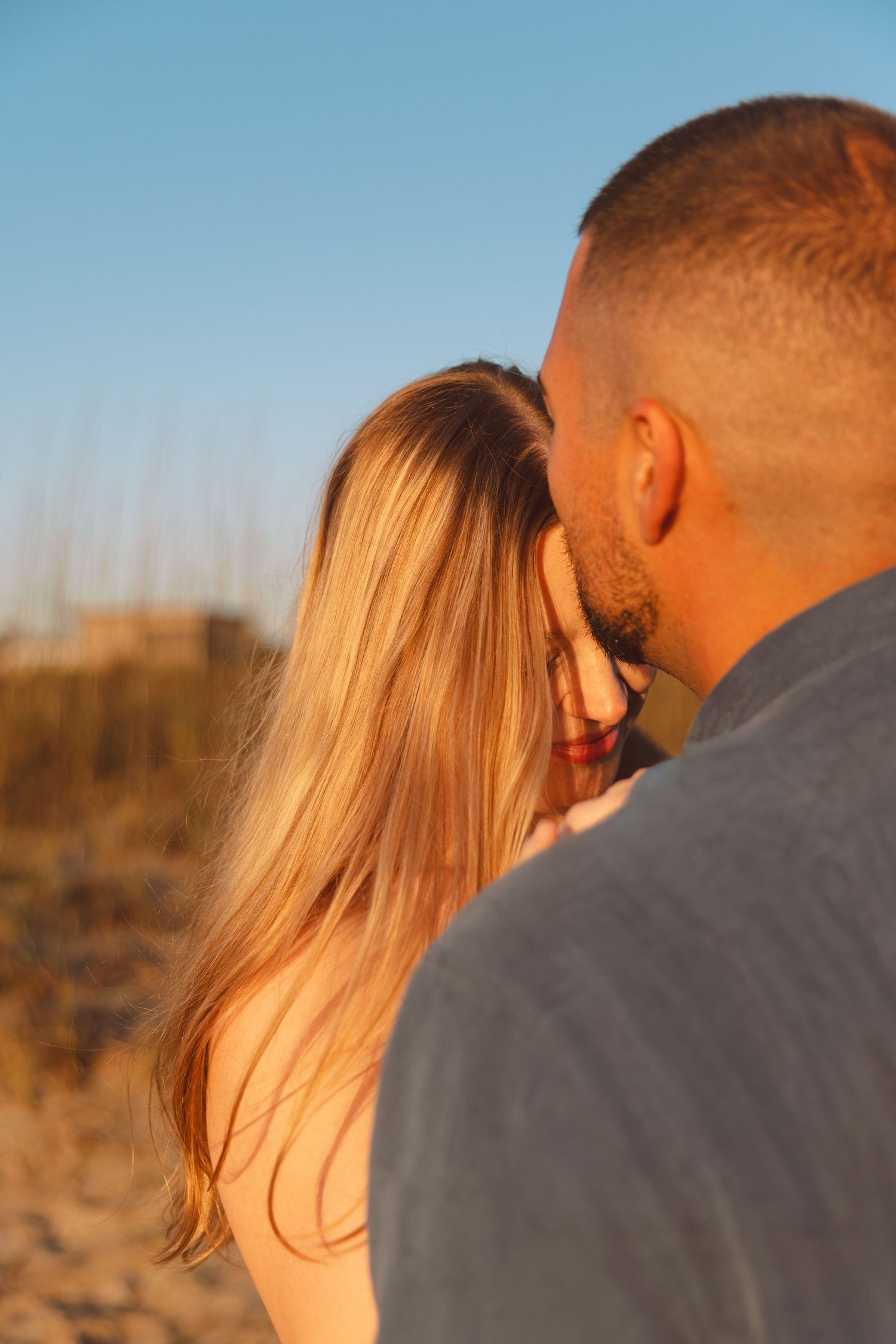 Couple sharing a romantic moment at golden hour on a sandy beach, with warm sunlight illuminating their faces.