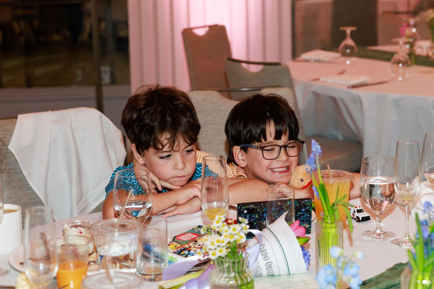 Two young boys sitting together at a decorated banquet table during a formal event.