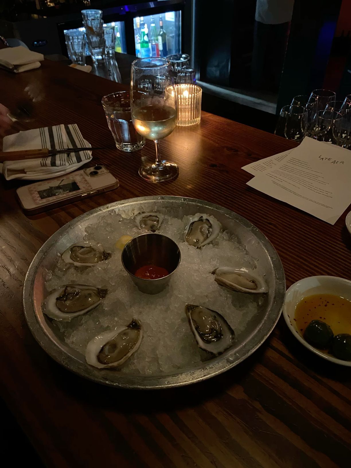 Fresh oysters on ice served on silver platter with cocktail sauce at dimly lit restaurant bar.