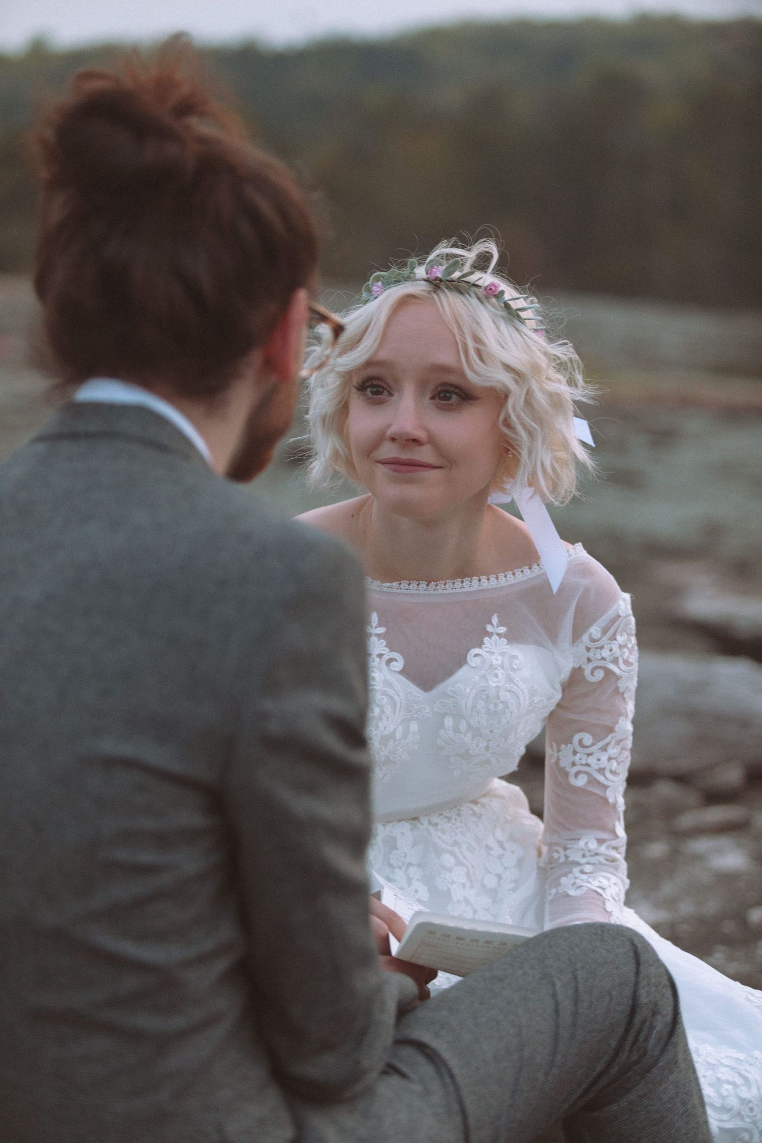 Emotional bride in floral crown gazing lovingly at groom during intimate outdoor wedding moment.