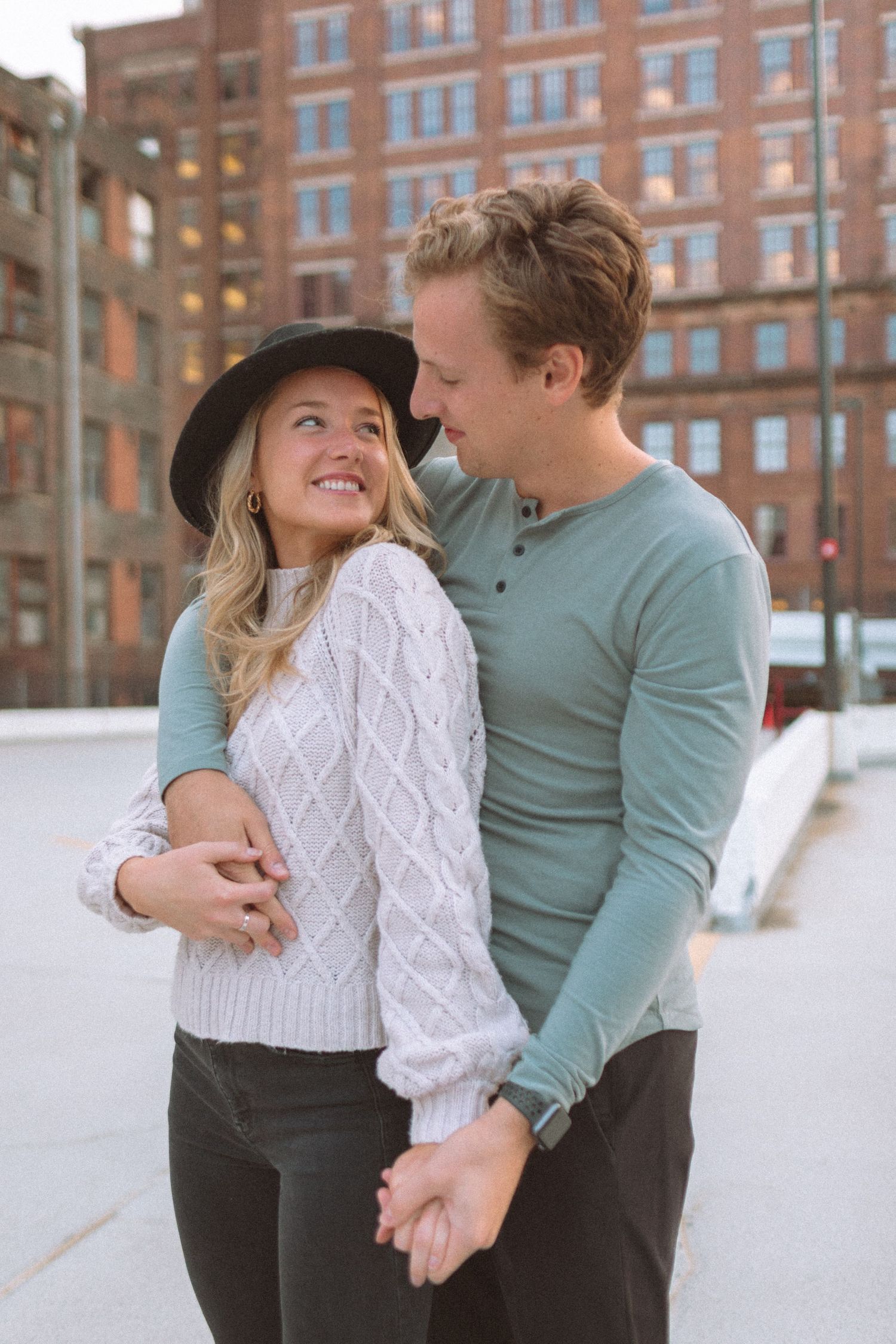Smiling couple embracing outdoors in urban setting, woman wearing black hat and knit sweater.