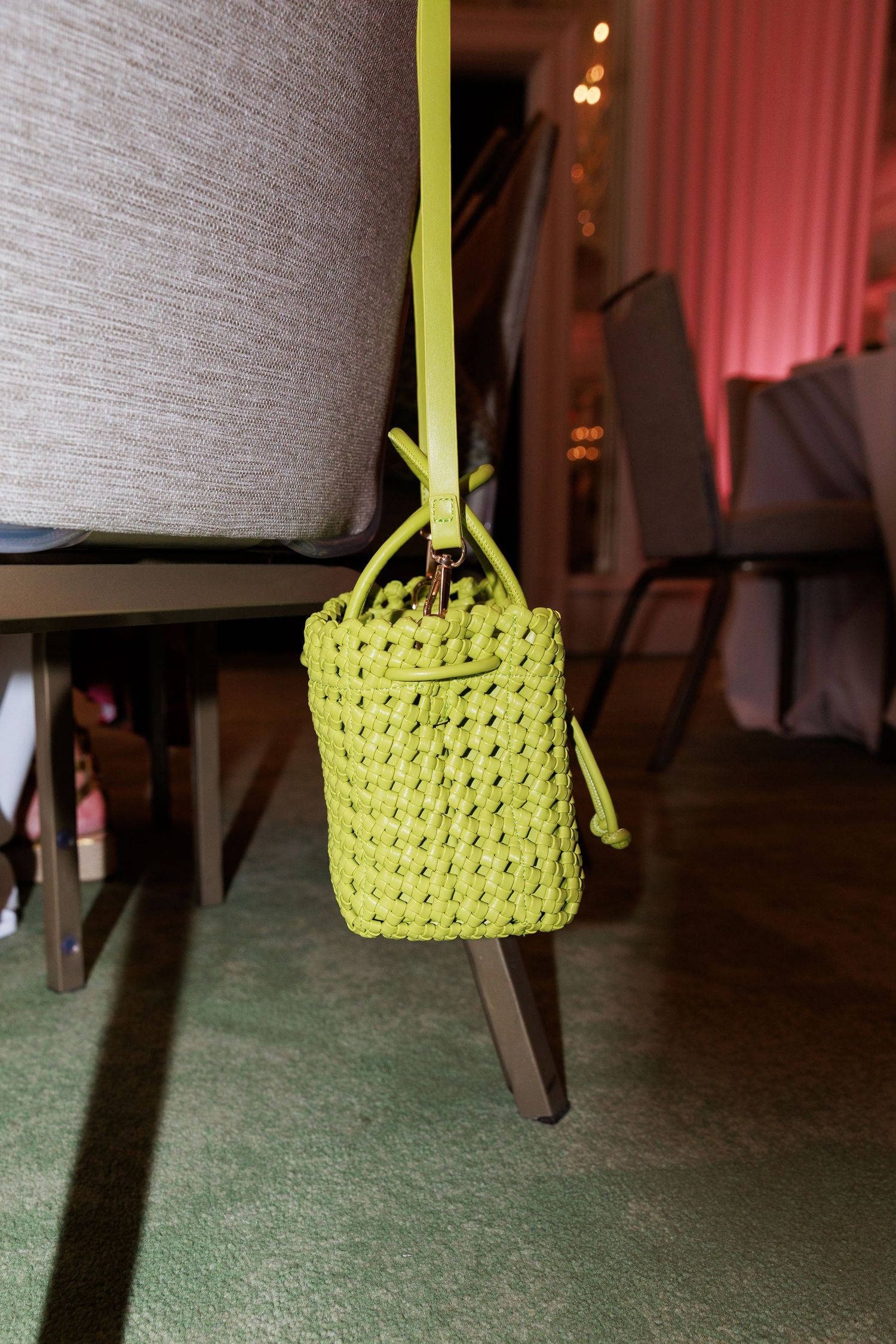 A lime green woven bucket bag hangs from a chair at an indoor event venue.