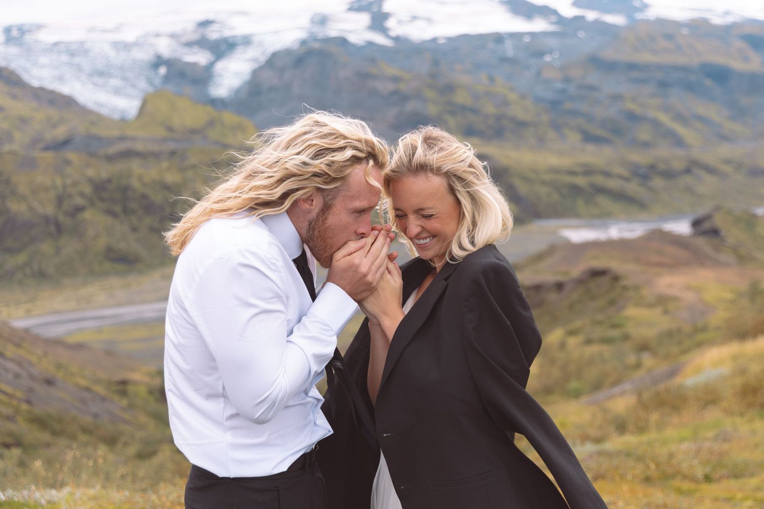 Two brides laughing joyfully during their Iceland elopement with glacial mountains in the background.
