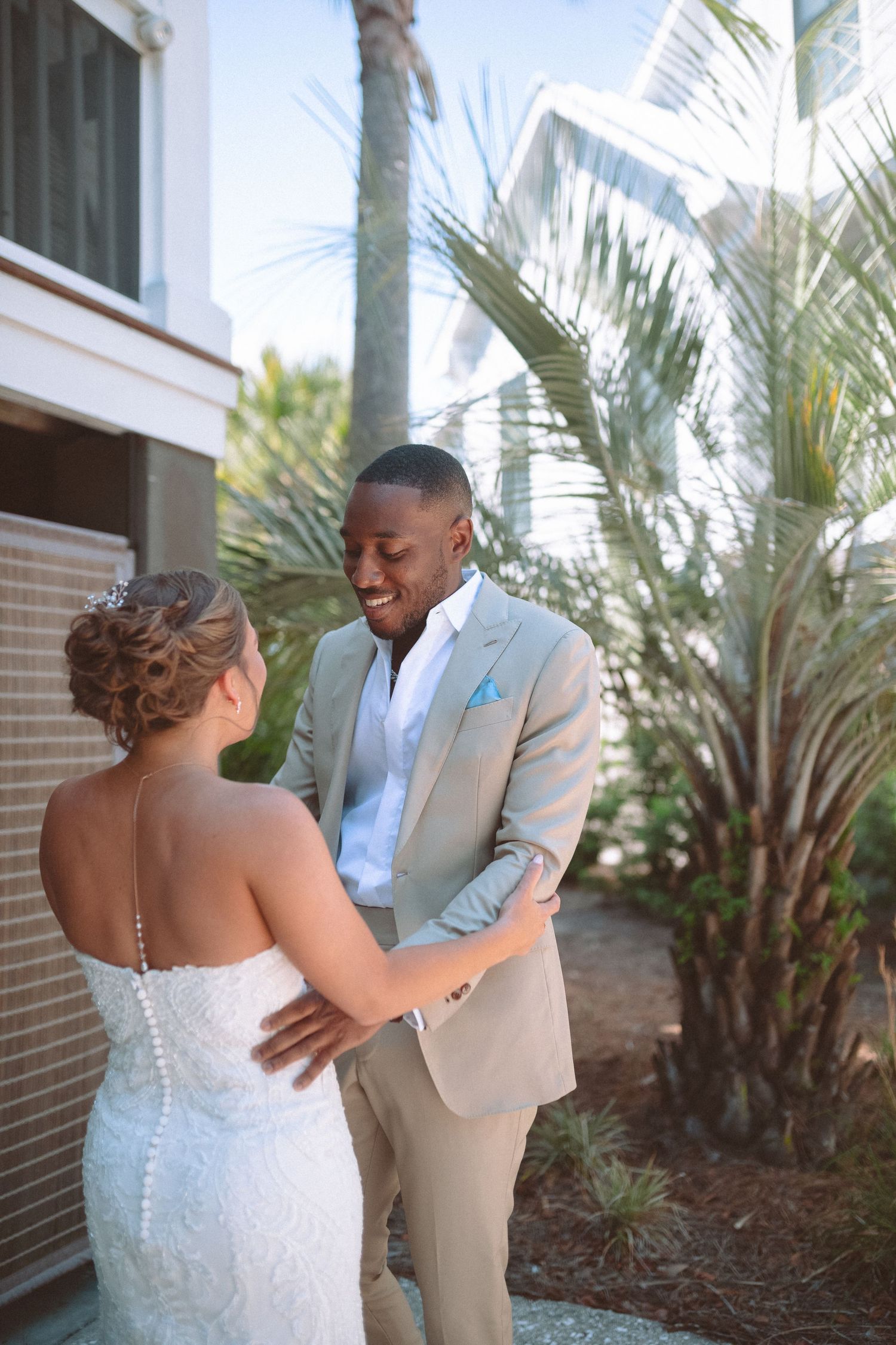 Bride and groom share an emotional first look moment, holding each other outdoors surrounded by tropical palms.