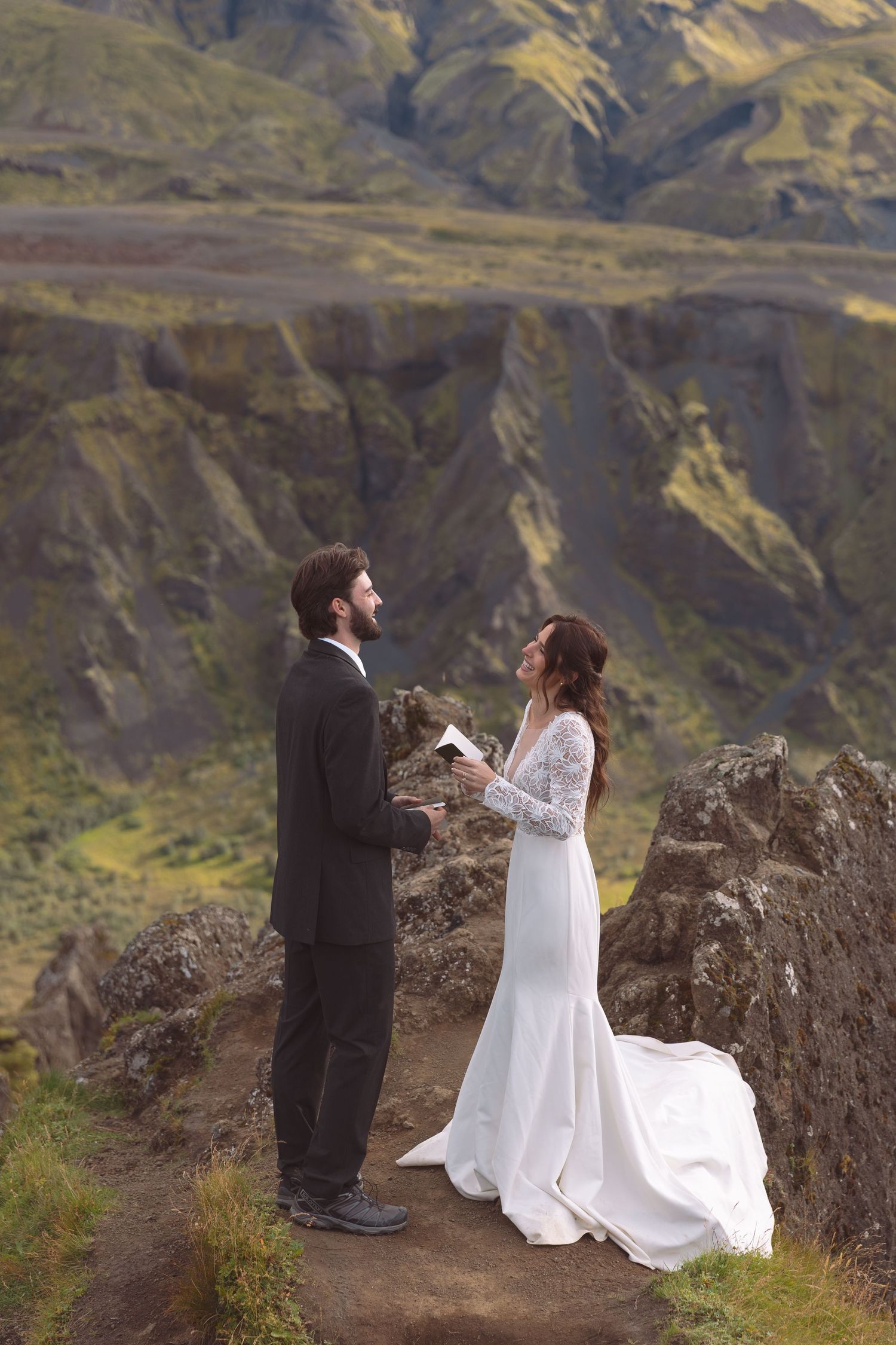 Groom reads wedding vows to smiling bride on a scenic Iceland mountain overlook during elopement.