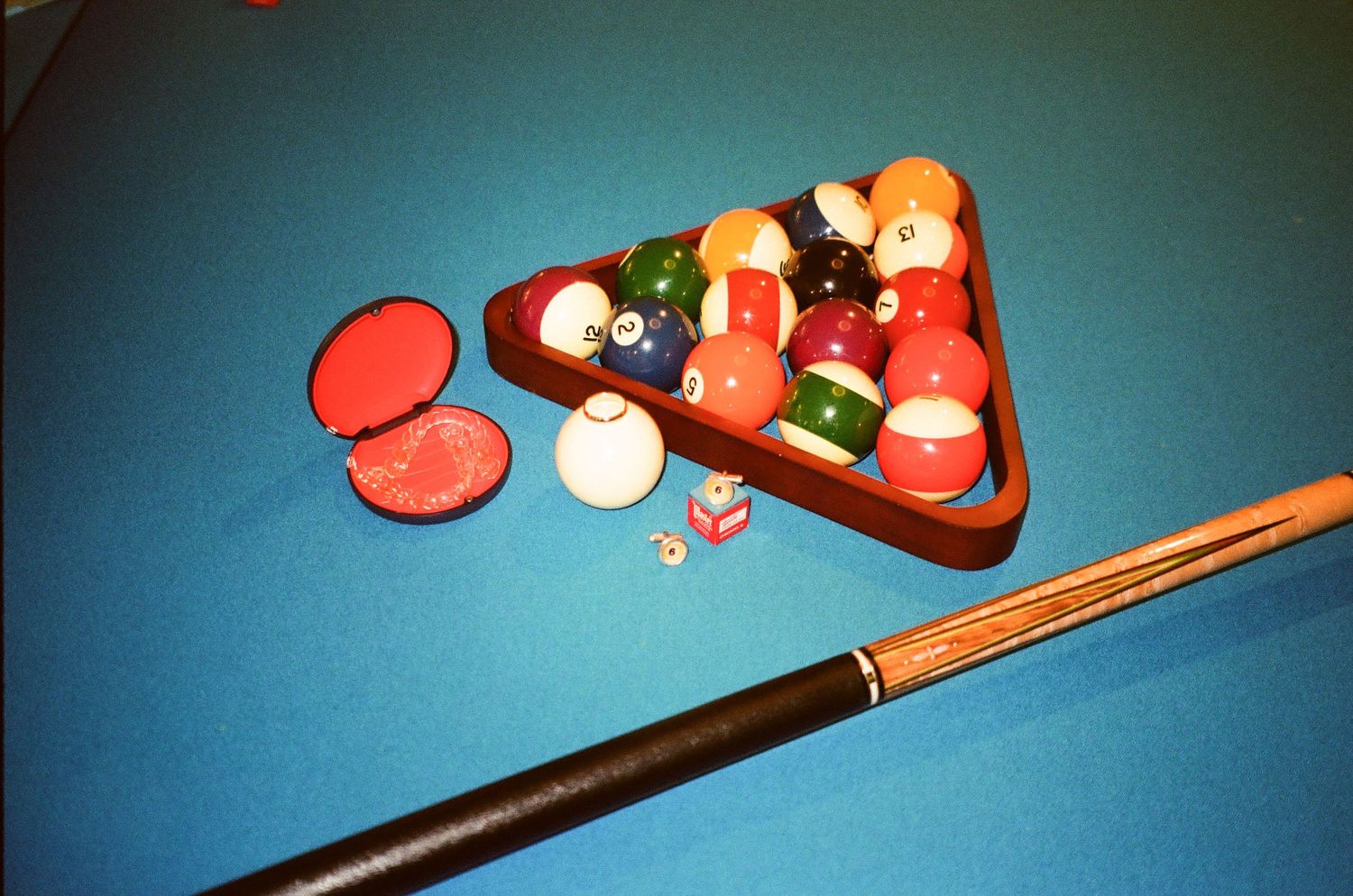 Billiard balls arranged in triangle rack on blue pool table with cue stick and red chalk holder.