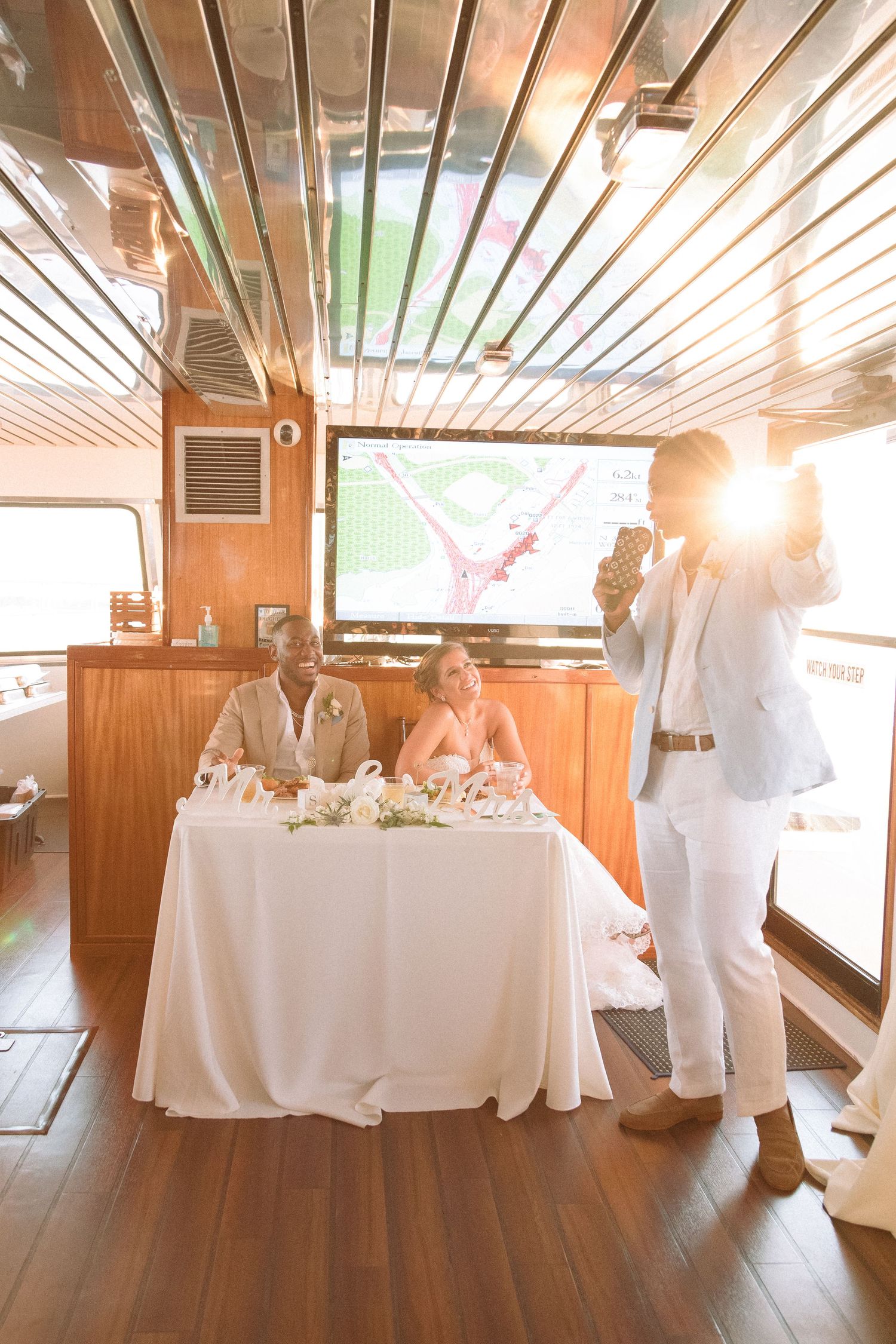 Wedding party member in white suit giving a toast to the newlyweds at their boat reception sweetheart table.