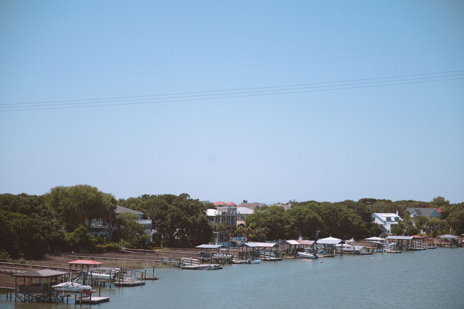 Waterfront homes and boat docks along a calm lake with lush green trees under a clear blue sky.