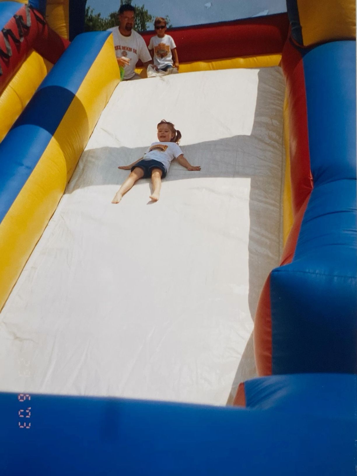 Young child sliding down a large inflatable bounce house slide at outdoor event.