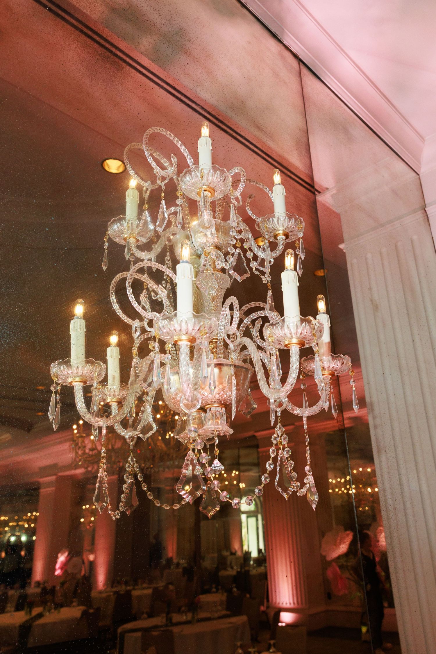 Elegant crystal chandelier with lit candle-style lights reflecting in a mirror at a formal event venue.