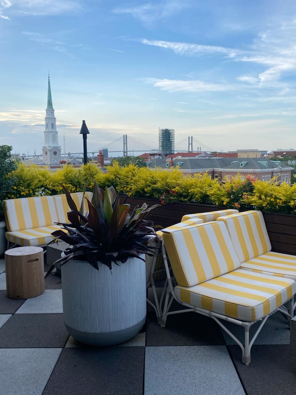 Rooftop terrace with yellow striped chairs, potted plants, and city skyline church view.