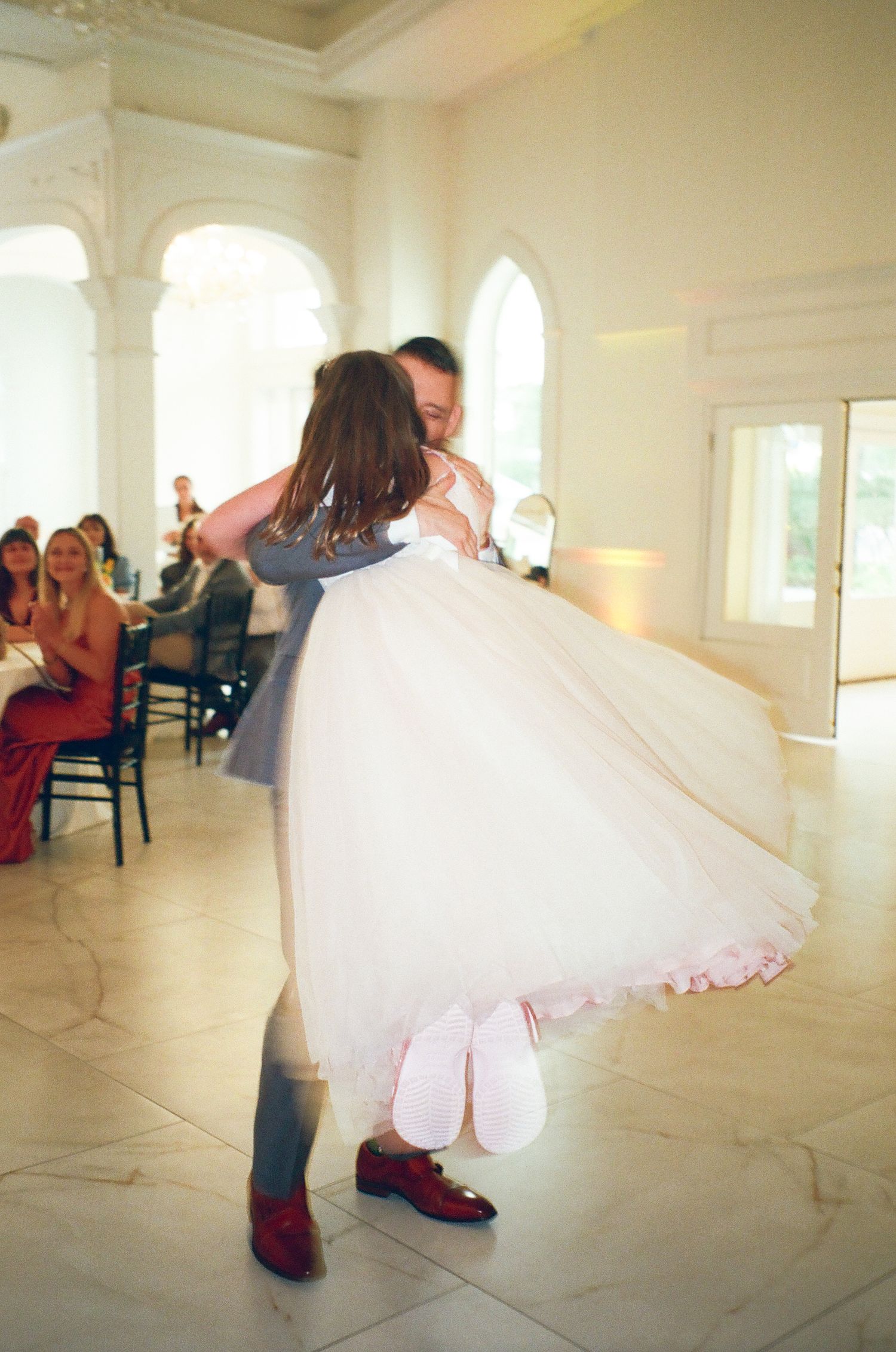Groom lifts bride in white tulle dress during romantic first dance at elegant wedding reception.