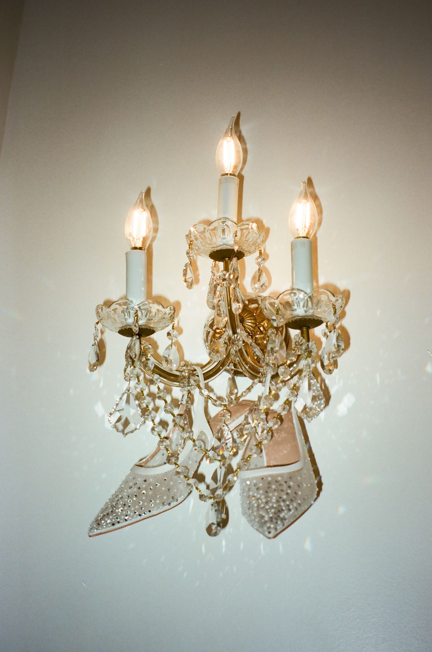 Crystal wall sconce with three candle lights and sparkling bridal heels draped elegantly among the chandelier crystals.