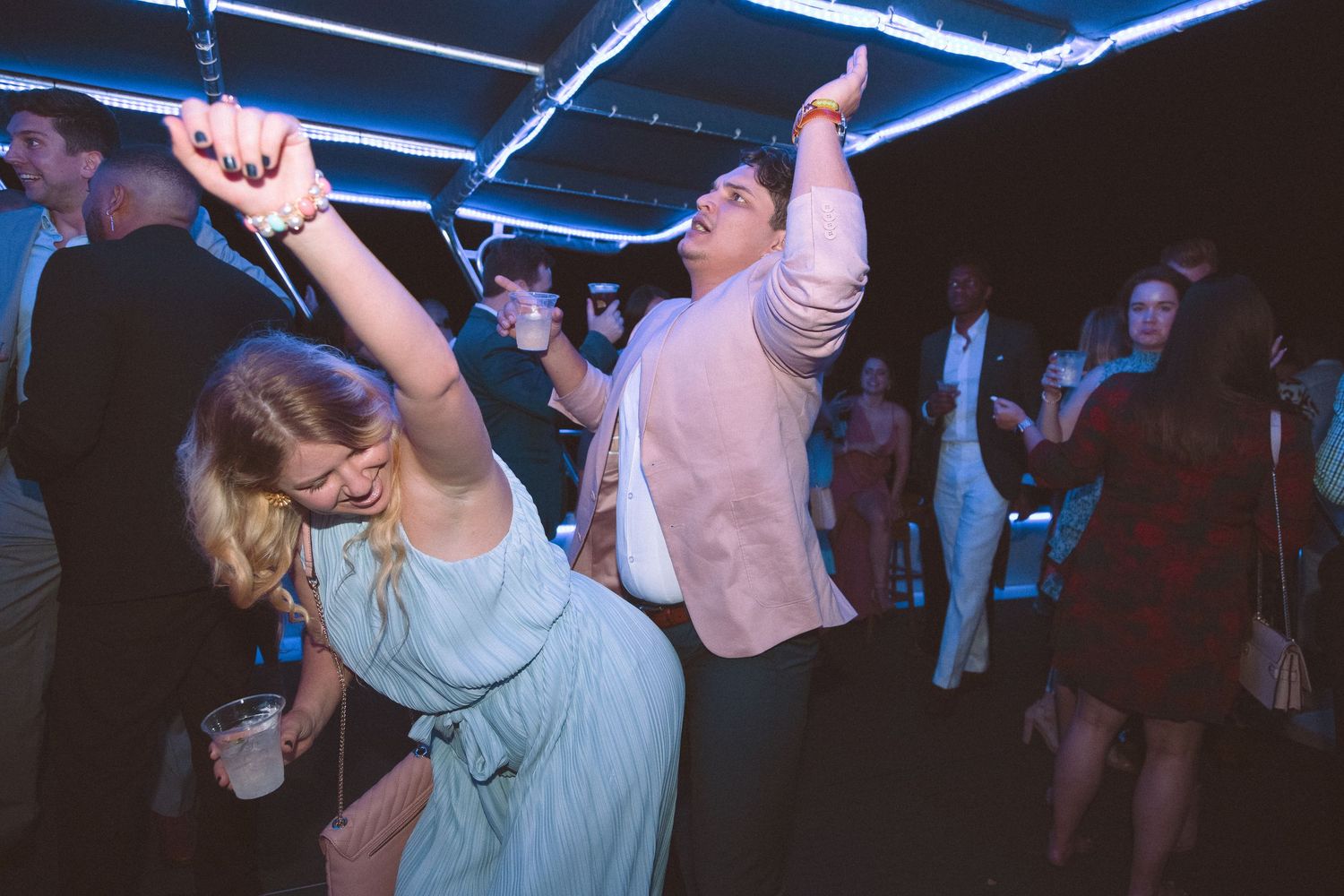 Couple dancing energetically at a wedding reception under blue neon lights.