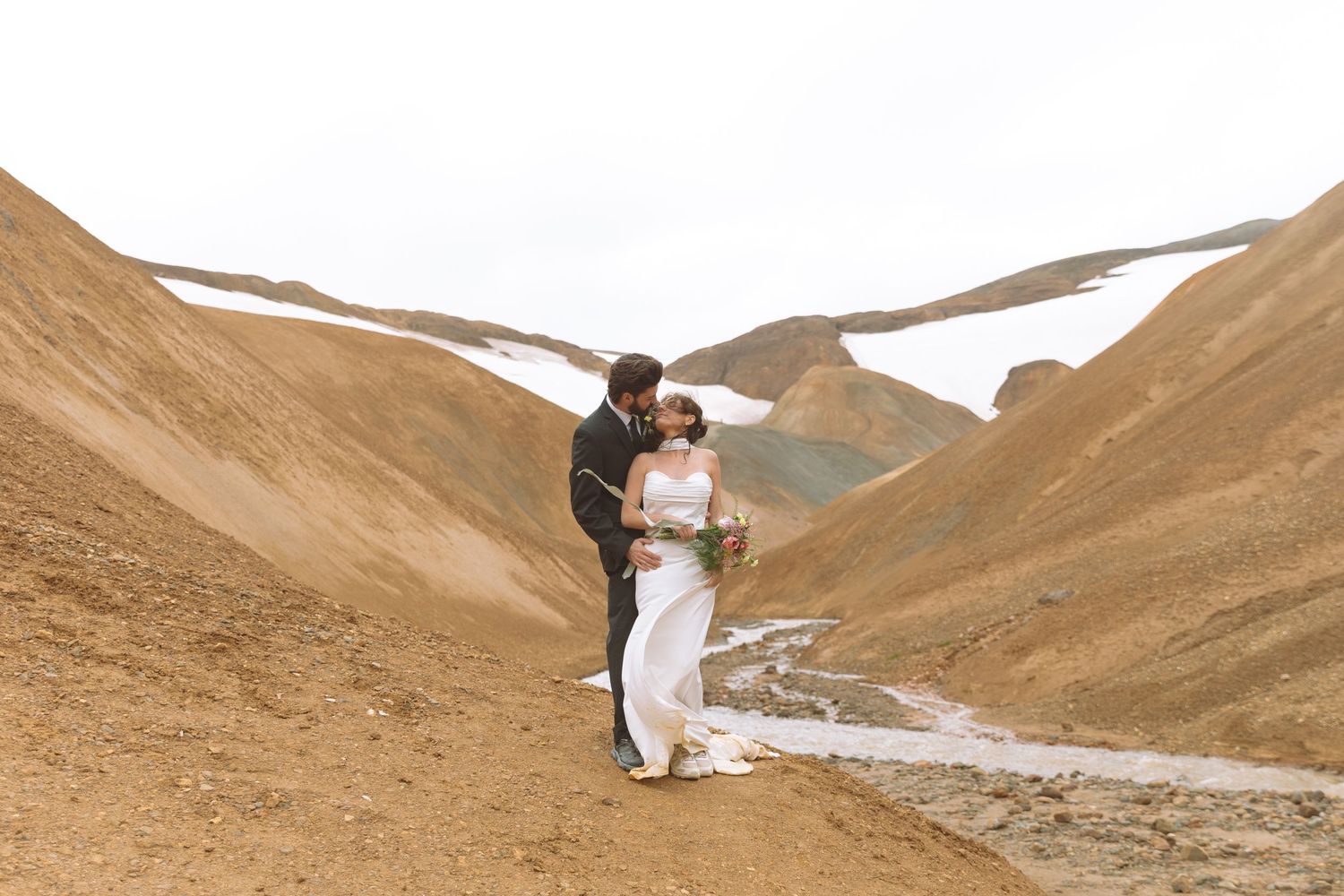 Bride and groom share an intimate embrace in a dramatic desert mountain valley on their wedding day.