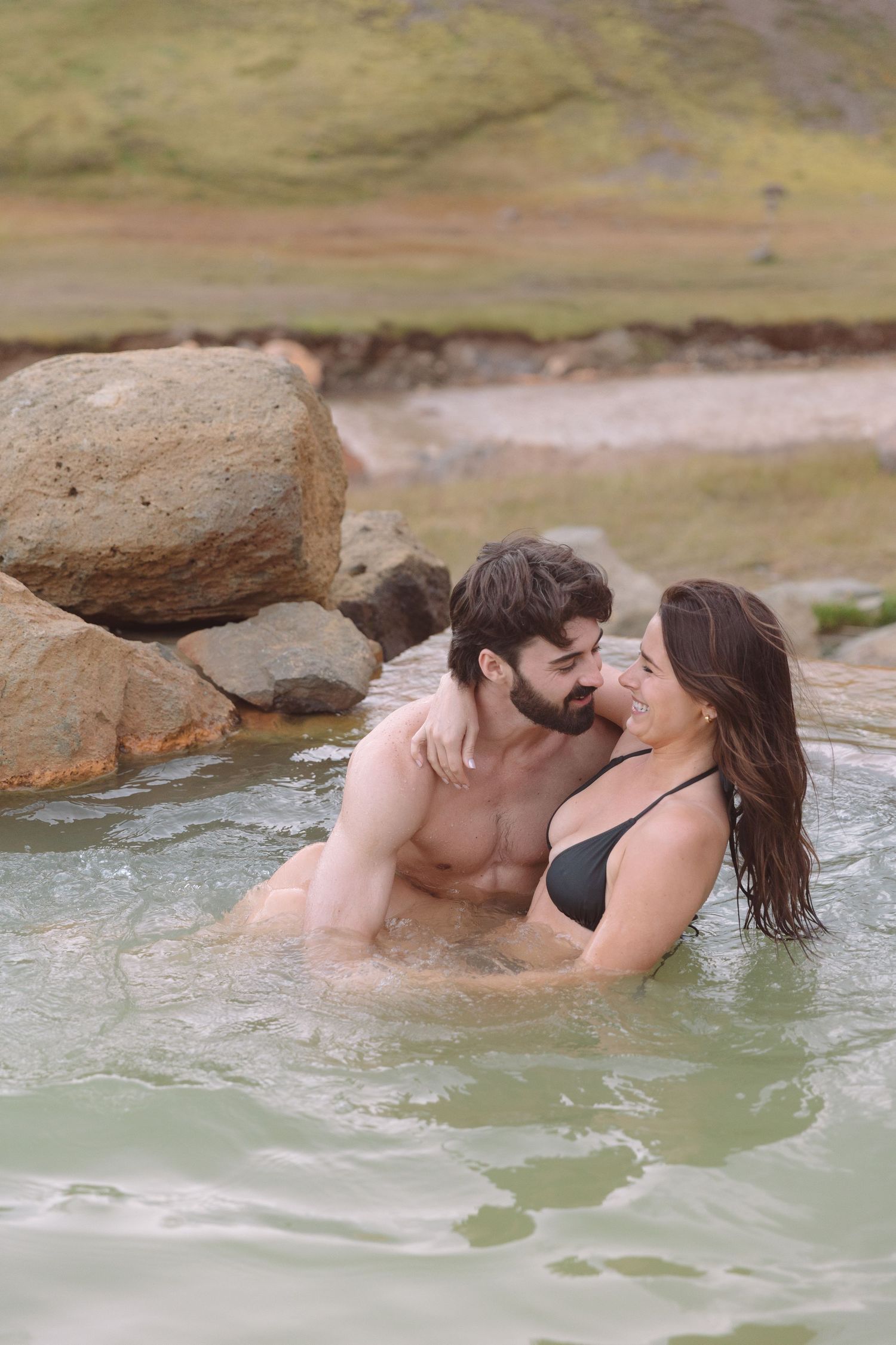 Romantic couple sharing an intimate moment while soaking in a natural geothermal hot spring in Iceland.