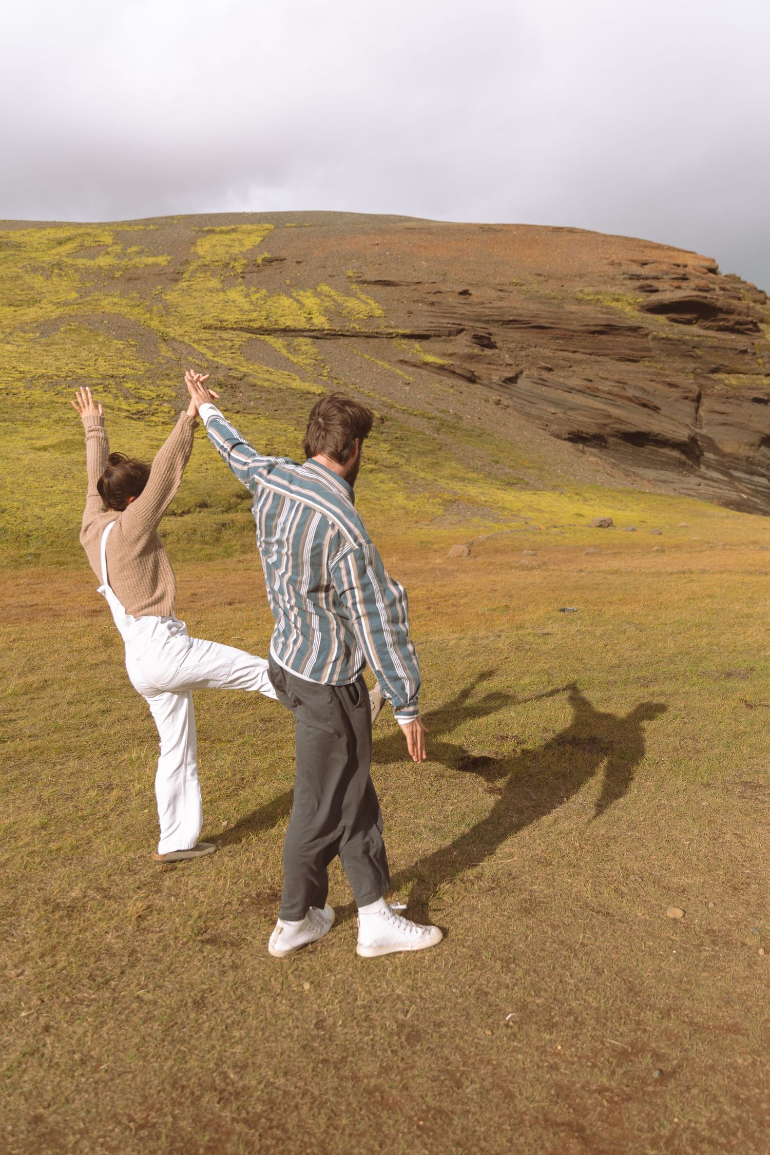 Couple holding hands and raising arms together on a scenic green Icelandic hillside landscape.