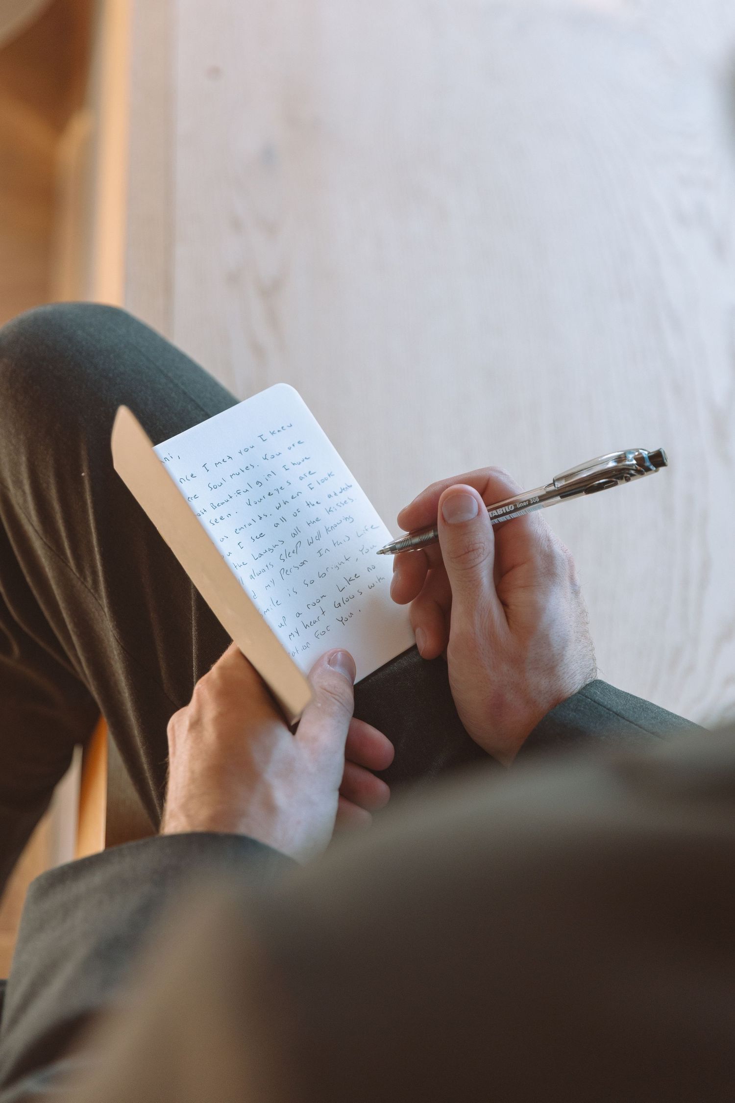 Overhead view of groom writing heartfelt wedding vows in notebook while seated indoors.