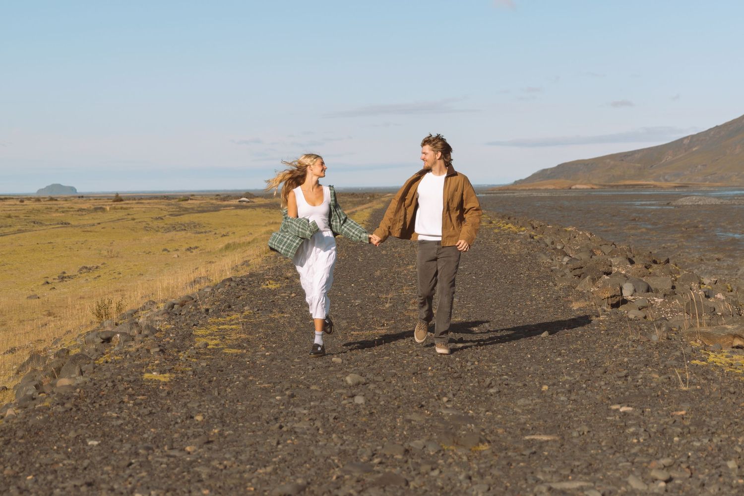 Couple holding hands walking on a volcanic black rock path with mountains in the distance.