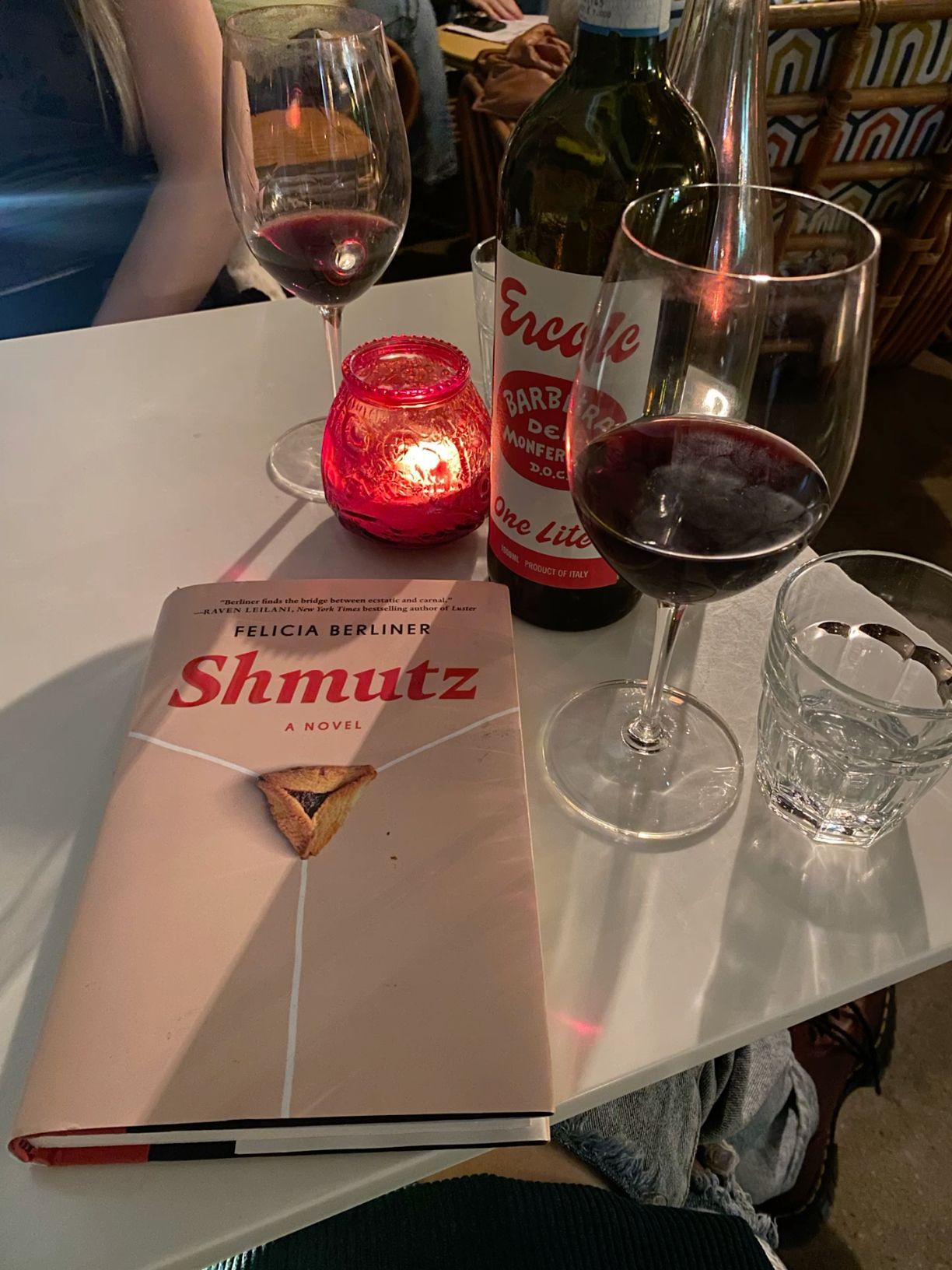 Book Shmutz by Felicia Berliner on table with red wine glasses and candle at cozy restaurant.